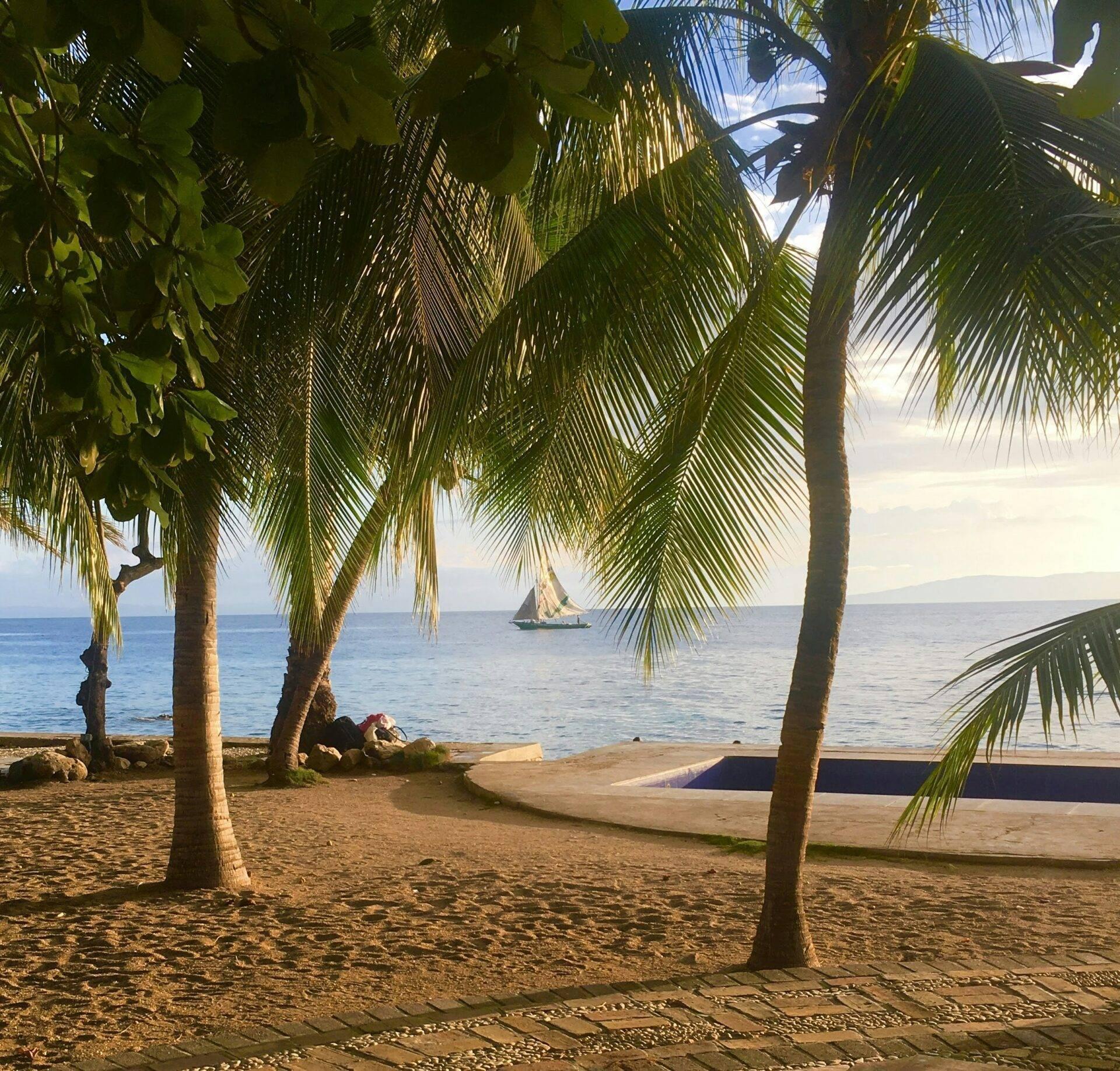 Plage tropicale avec palmiers, bateau à voile au large et pirogue échouée sur le sable