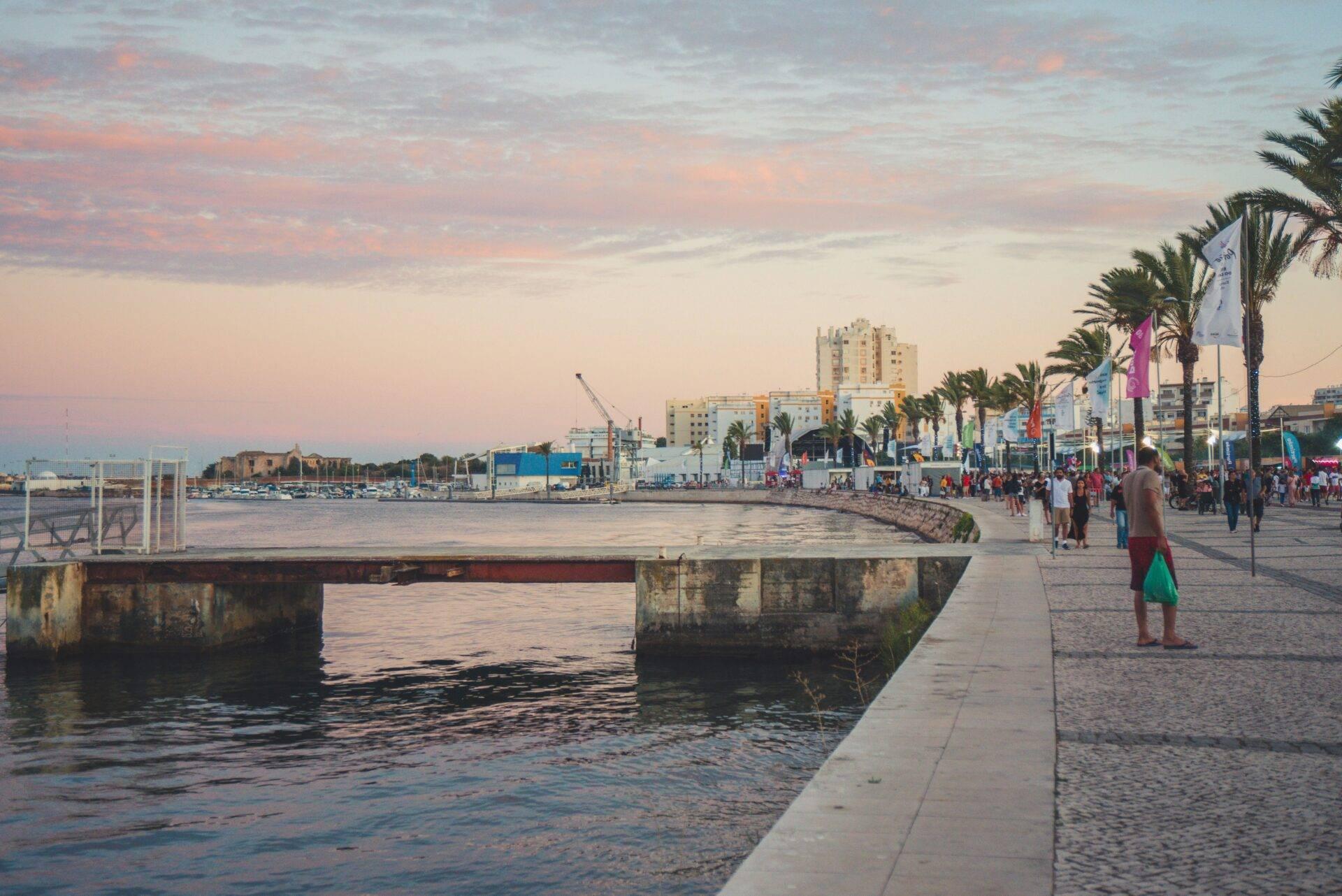 Une promenade littorale animée au coucher du soleil avec palmiers, architecture moderne et port maritime en arrière-plan