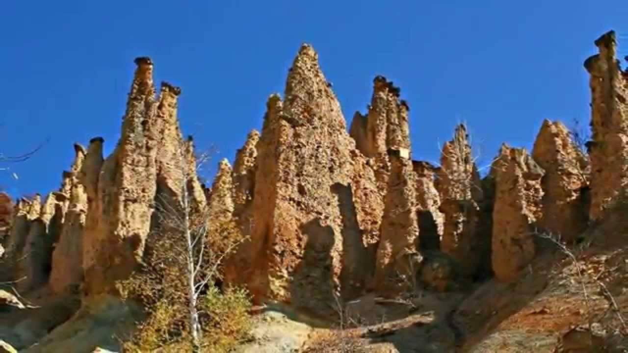Formation rocheuse spectaculaire avec pics de grès ocre et végétation clairsemée sous ciel bleu dégagé