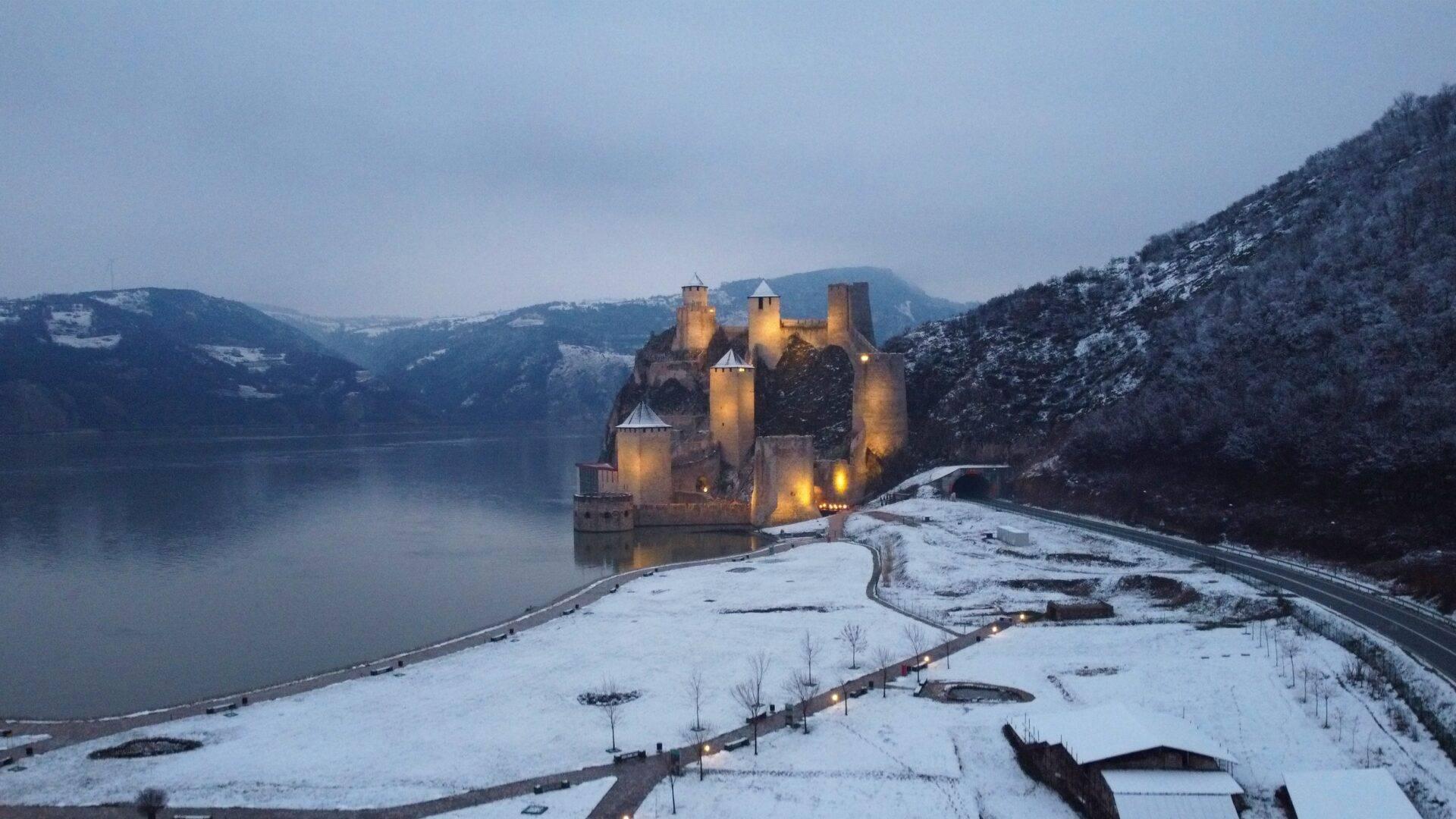 Un château médiéval illuminé au crépuscule sur une presqu’île rocheuse dominant un lac gelé en hiver