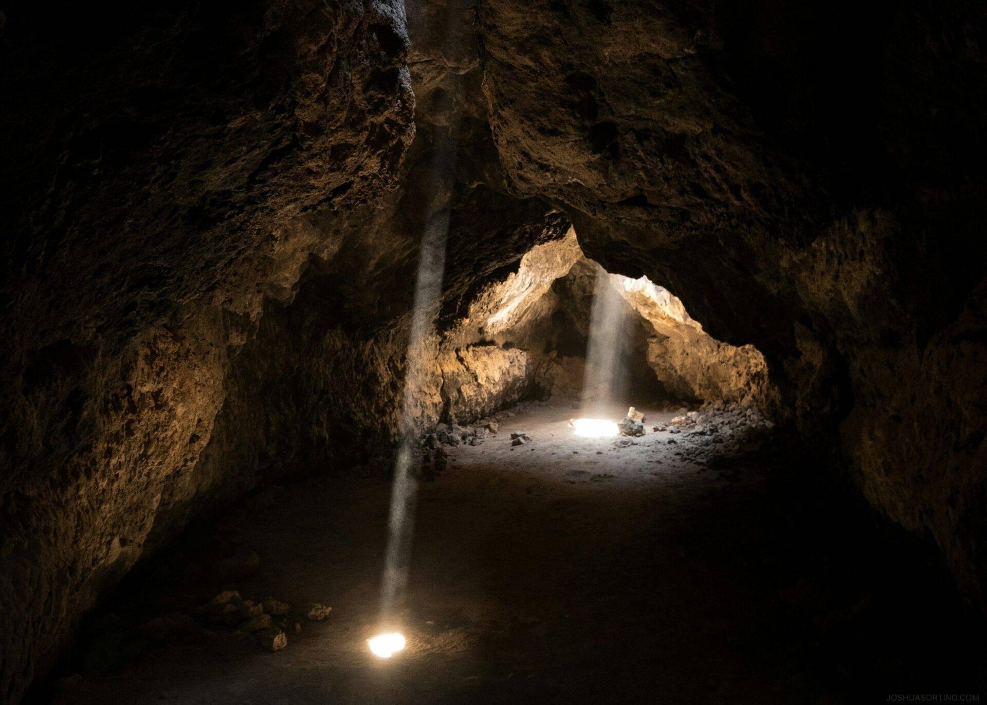 Intérieur d’une grotte calcaire avec rayons de lumière traversant l’obscurité et vue sur l’entrée illuminée