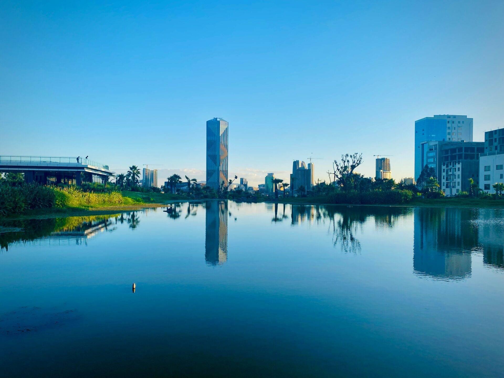 Skyline urbaine moderne reflétée dans les eaux calmes d’une rivière avec végétation et pont
