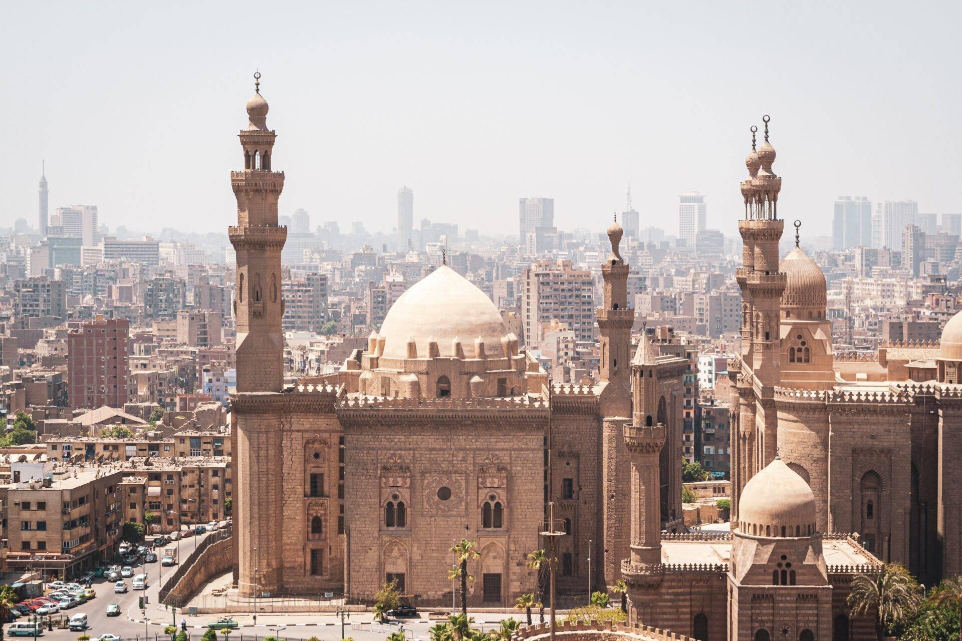 Vue aérienne d’une mosquée historique avec dômes blancs et minarets, dominant un quartier urbain dense