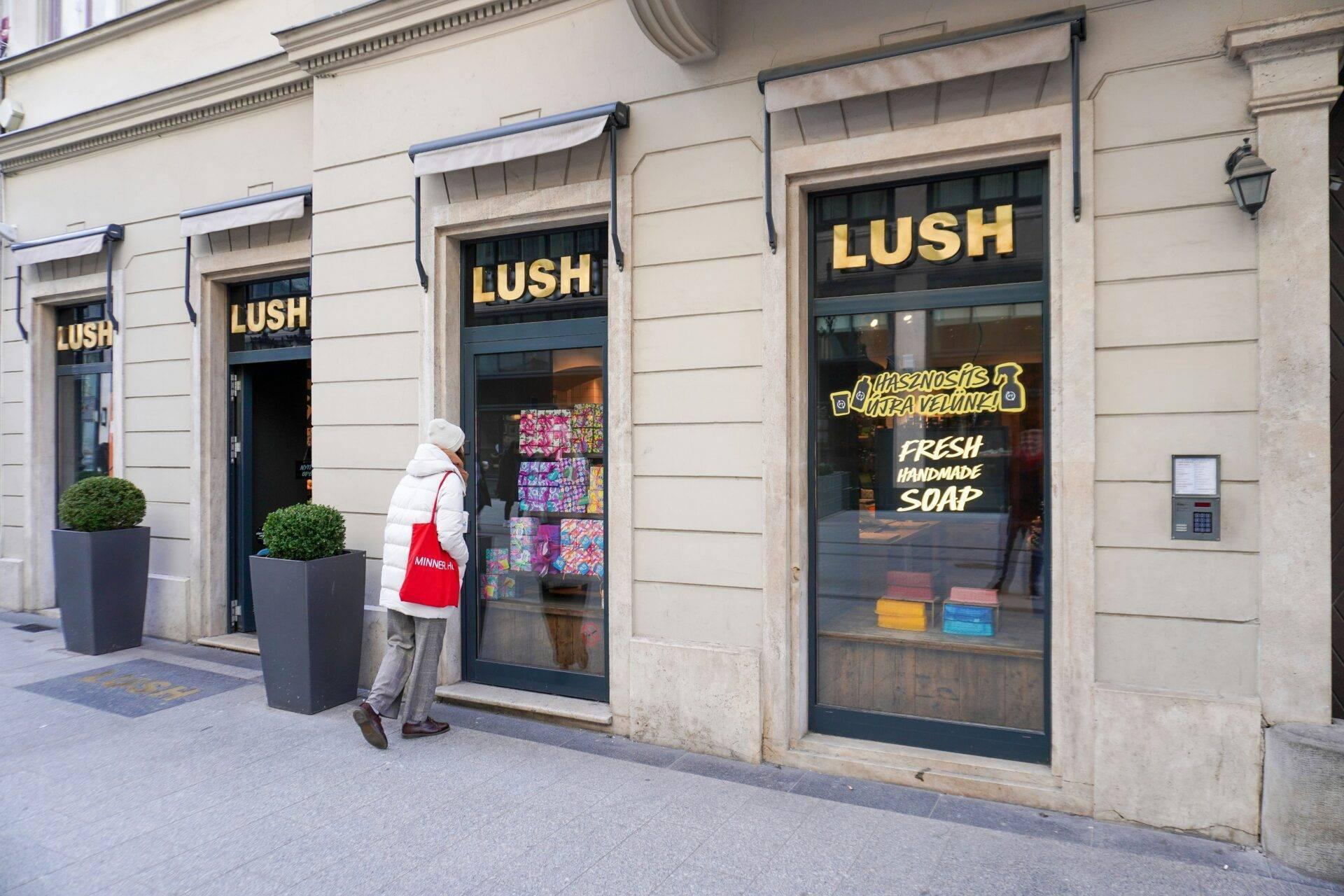 Une femme devant une boutique de cosmétiques artisanaux “Lush” dans une rue pavée européenne avec façade classique
