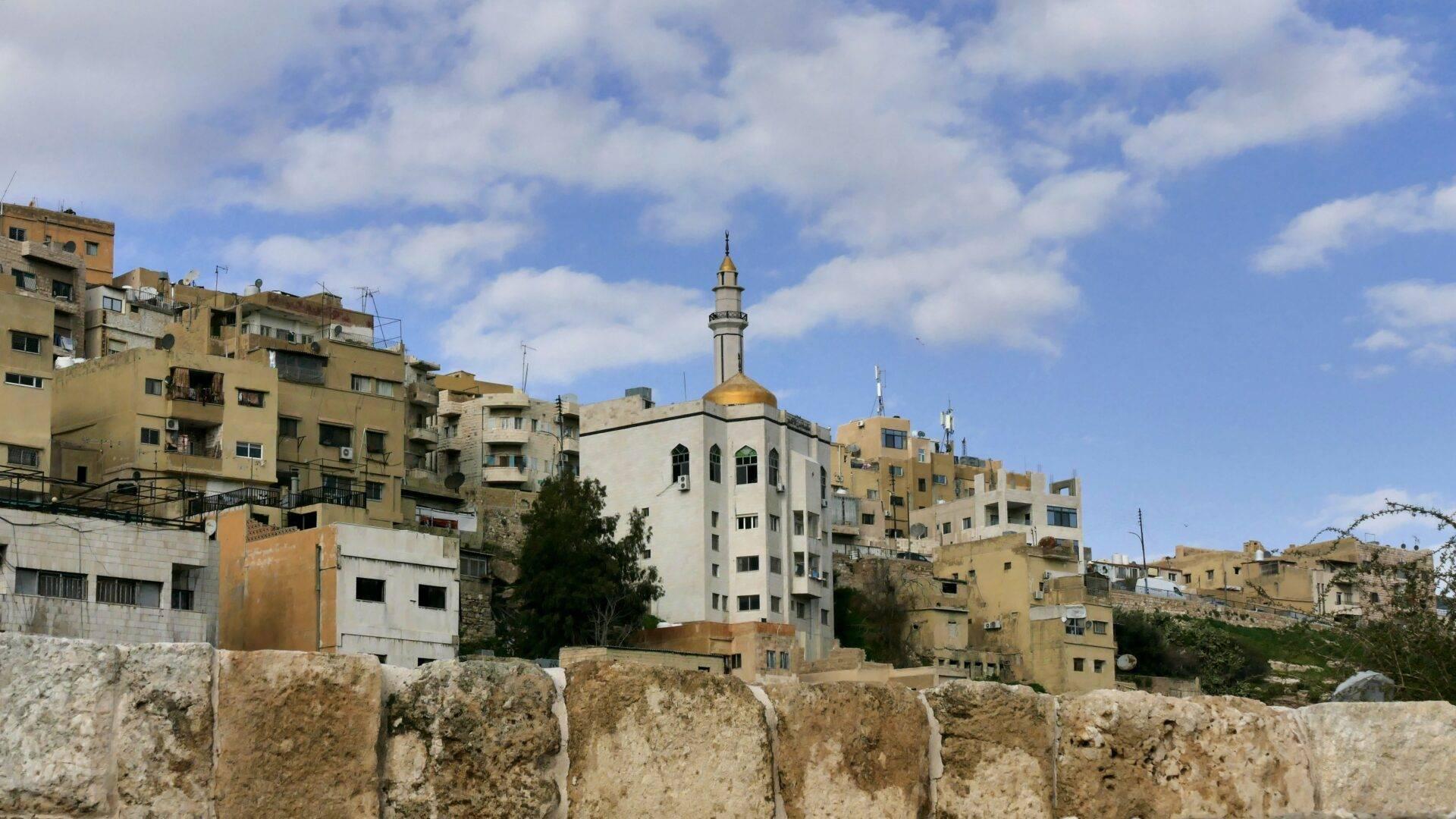 Vue d’une ville du Moyen-Orient avec mosquée à dôme doré entourée d’immeubles en pierre beige et mur de fortification