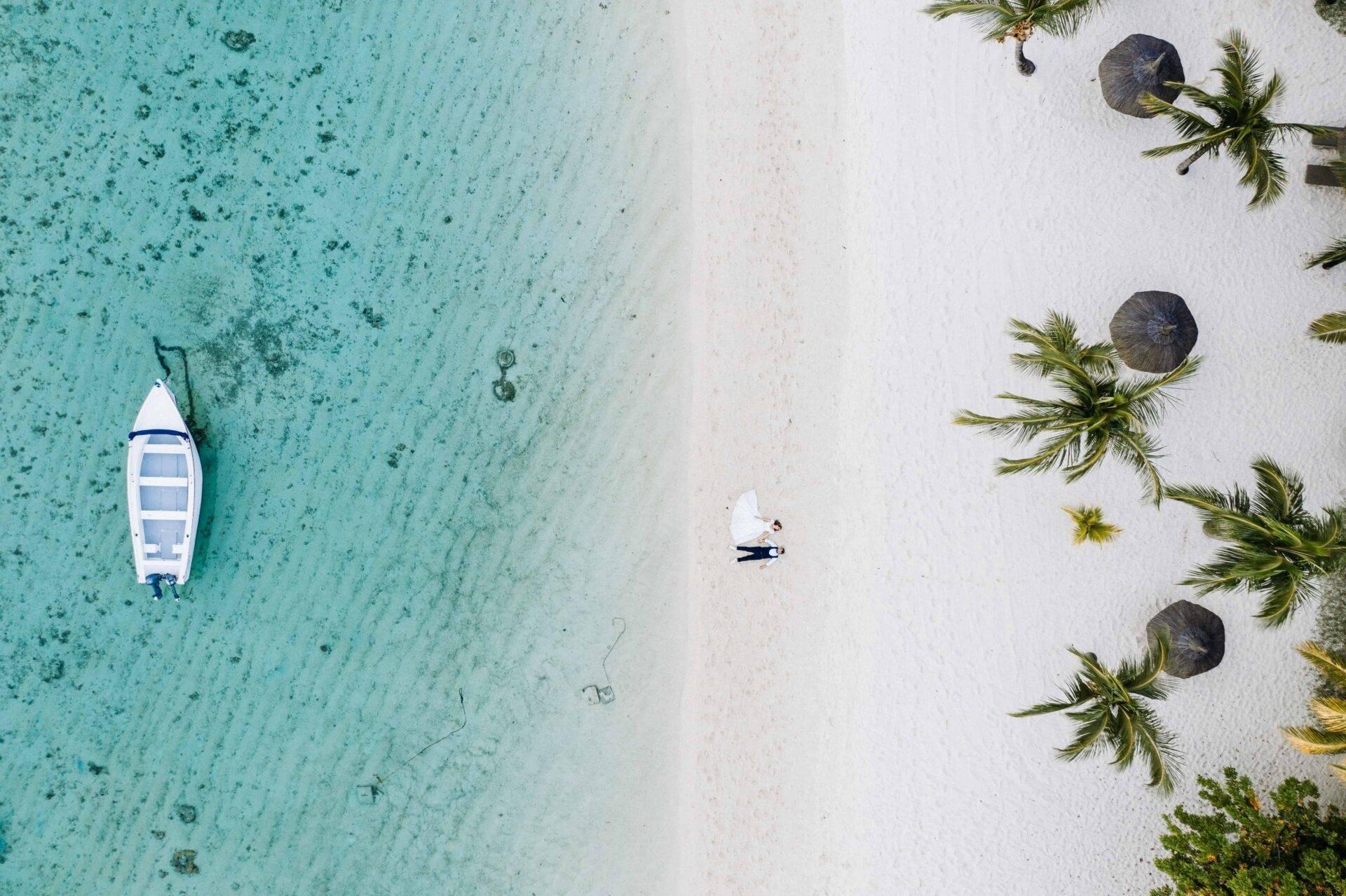 Vue aérienne d’une plage tropicale avec un bateau blanc ancré, du sable blanc et des palmiers