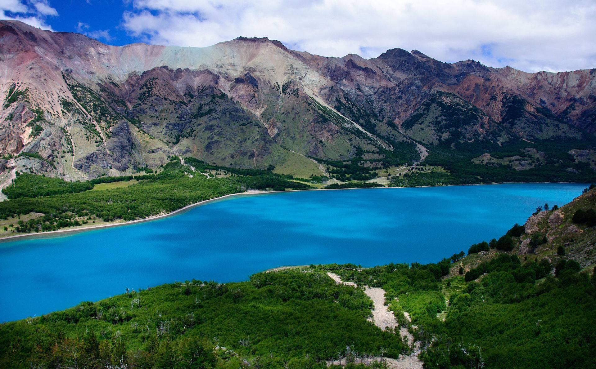Un lac alpin d’un bleu turquoise intense encadré de montagnes colorées et de végétation verte luxuriante
