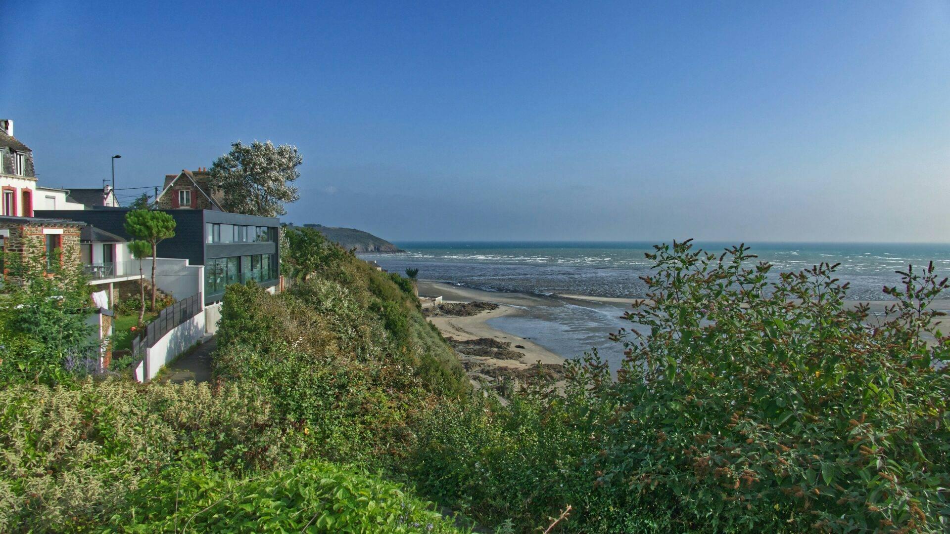 Maisons côtières modernes et traditionnelles surplombant une plage rocheuse et la mer sous un ciel bleu dégagé