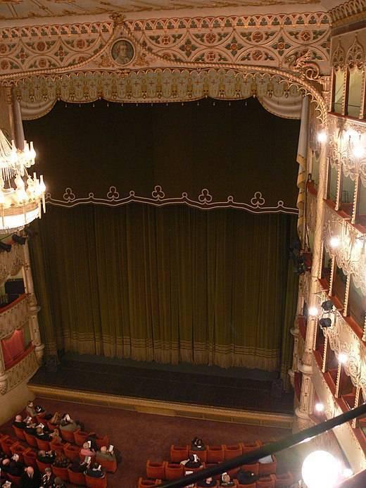 Intérieur ornementé d’un théâtre historique avec rideau vert foncé et balcons illuminés