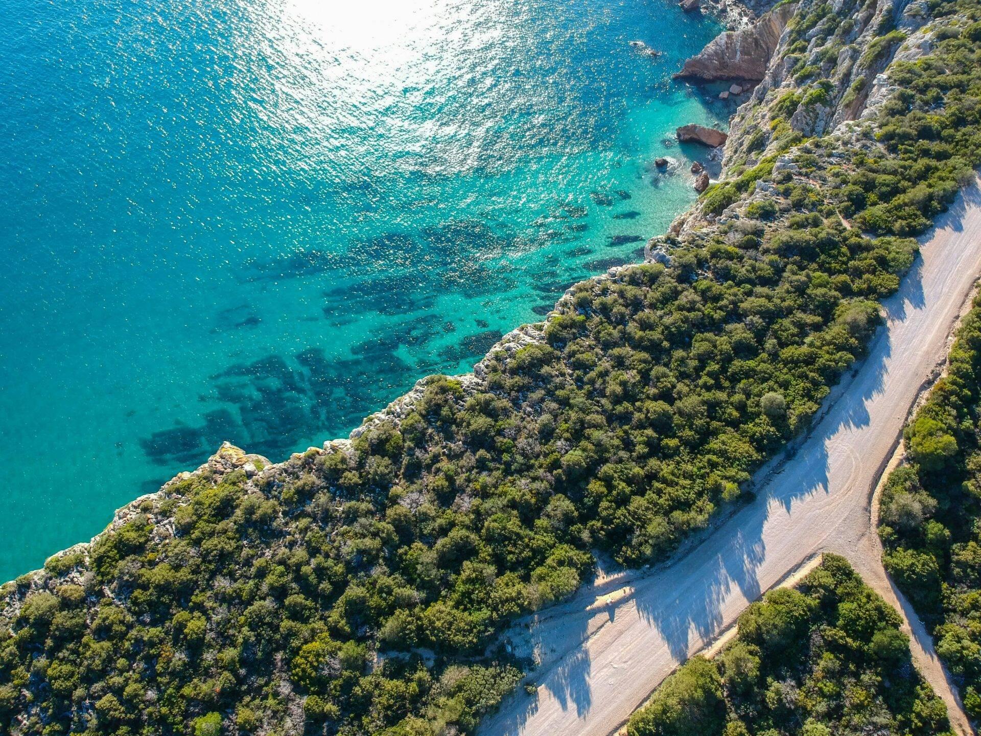 Vue aérienne d’une côte méditerranéenne avec falaises boisées, plage de sable et eaux turquoise cristallines