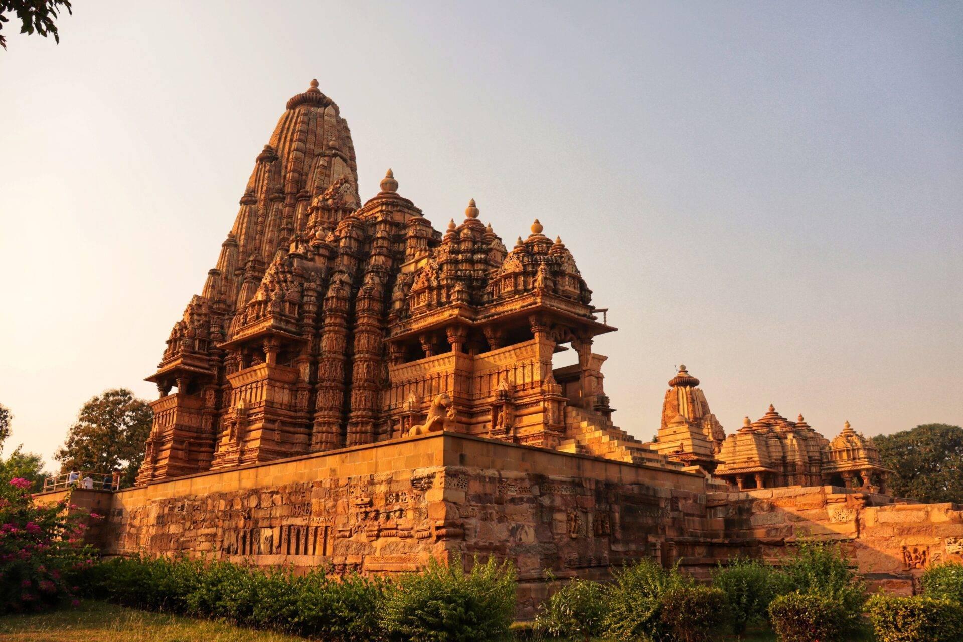 Temple hindou en grès rouge avec tours ornementées et sculptures détaillées, illuminé par la lumière du coucher de soleil