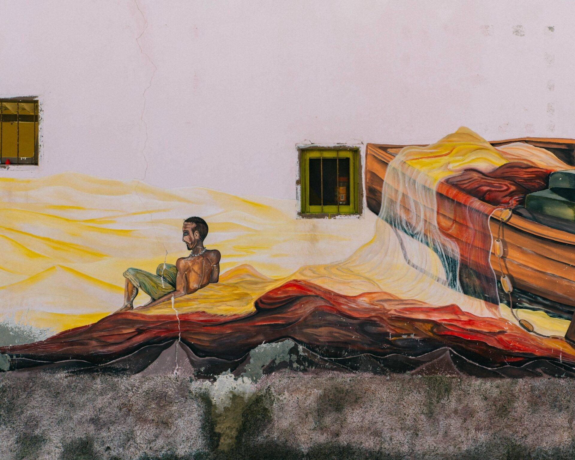 Fresque murale colorée représentant un pêcheur et des bateaux traditionnels sur façade blanche côtière