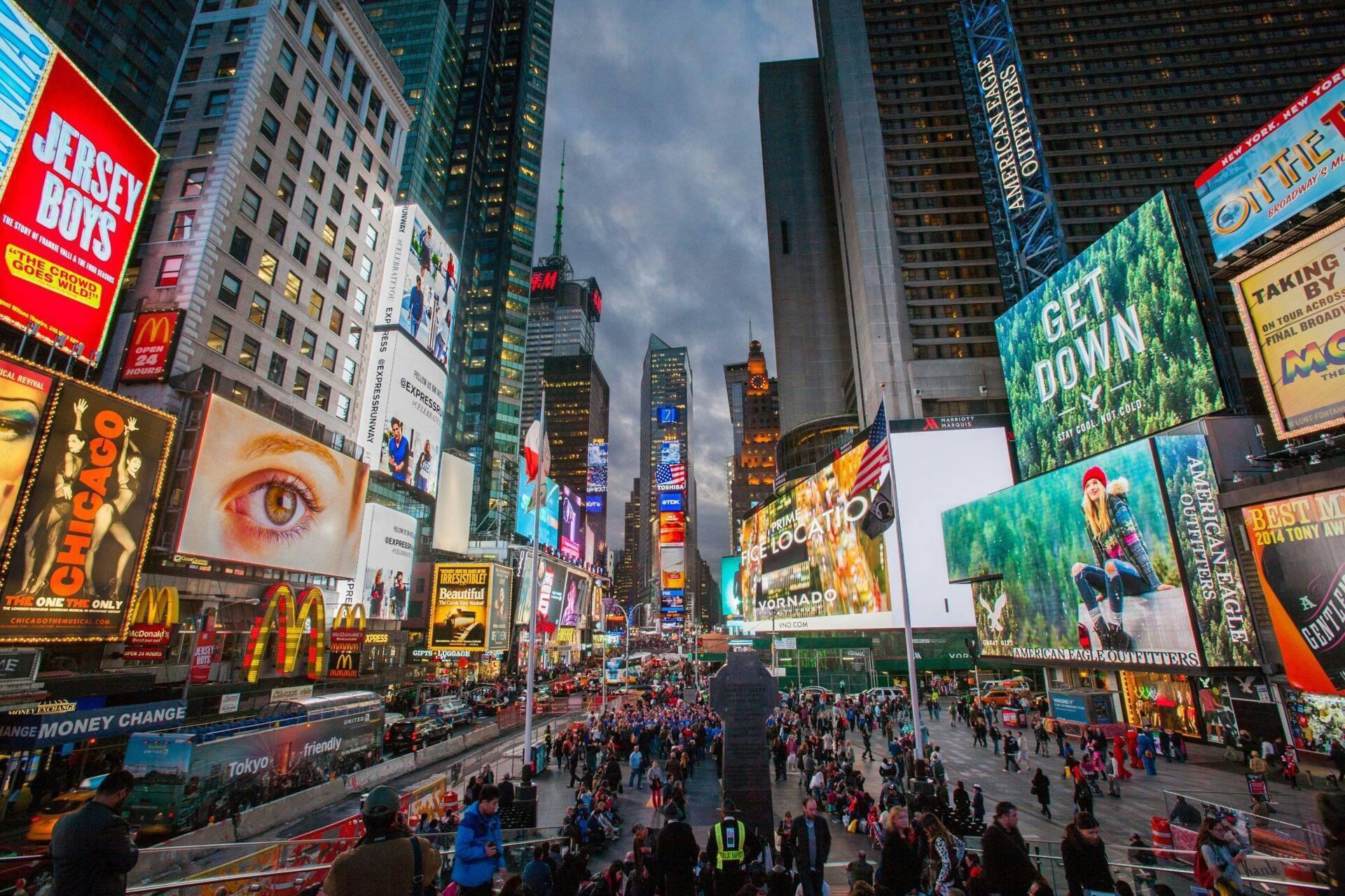 Une place urbaine animée avec gratte-ciel, écrans géants et foule dense de touristes et passants