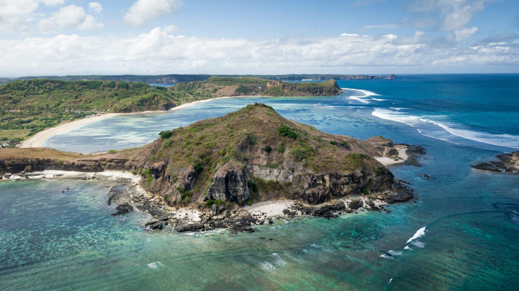 Vue aérienne d’une île rocheuse verdoyante entourée de plages de sable blanc et d’eaux turquoise sous ciel dégagé