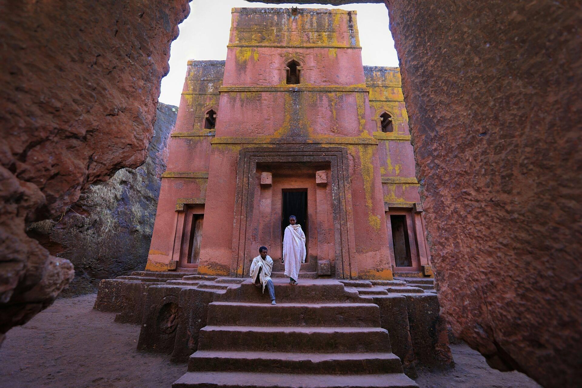 Église monolithe rouge avec façade ornementée, visiteurs en vêtements traditionnels devant l’entrée principale