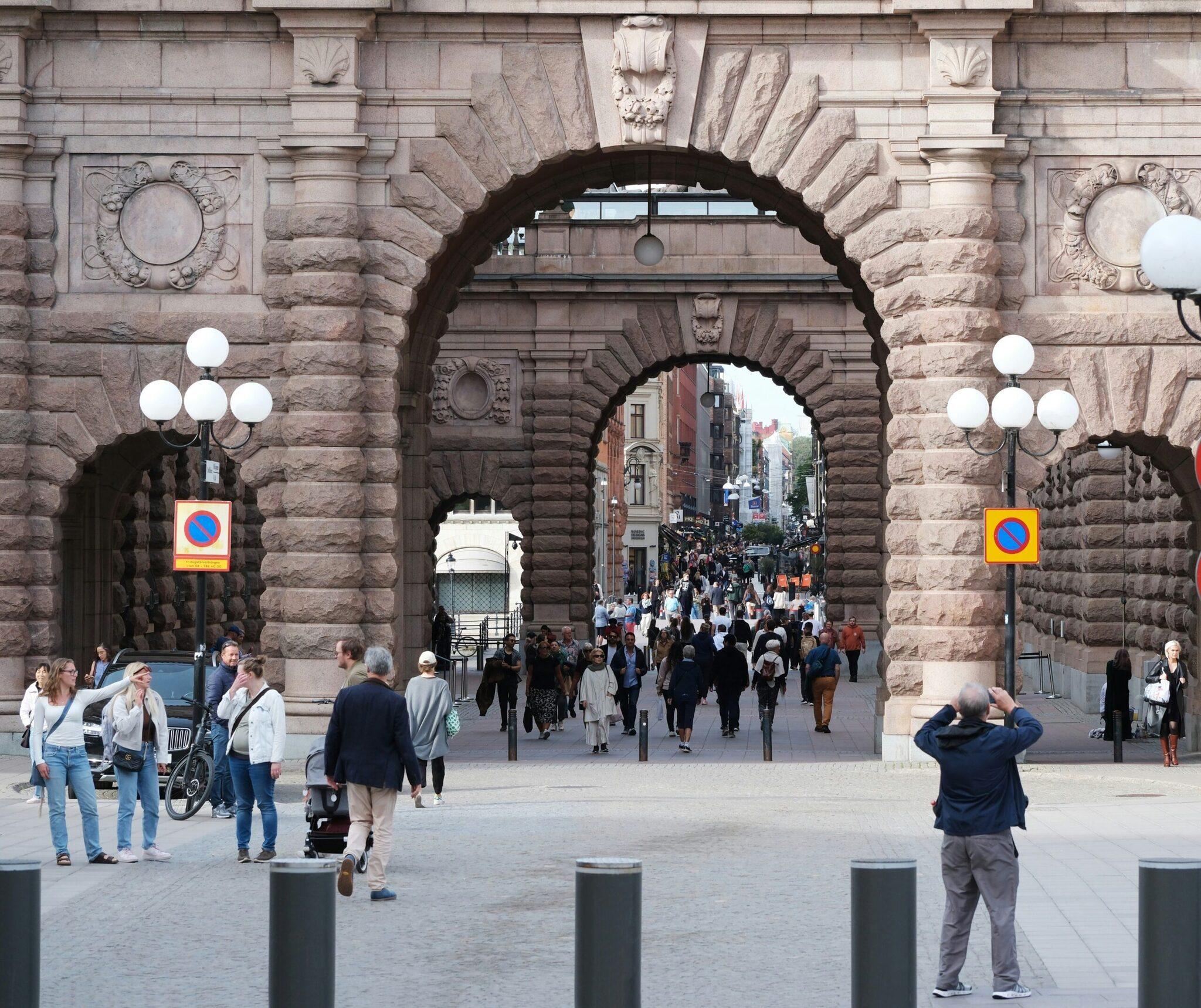Une rue piétonne animée traversant une imposante arche de pierre historique avec des bâtiments en briques en arrière-plan