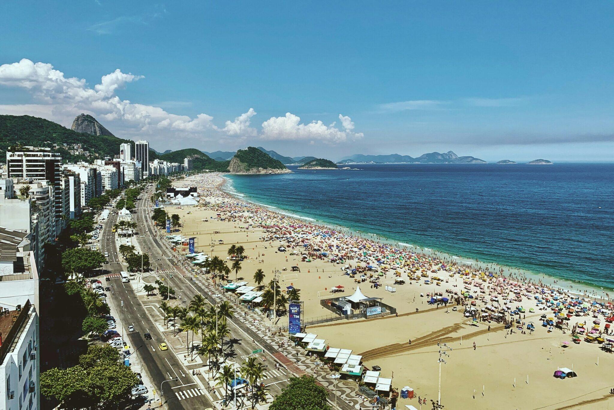 Vue aérienne d’une plage urbaine bondée avec ses immeubles, promenade littorale et montagne verdoyante en arrière-plan
