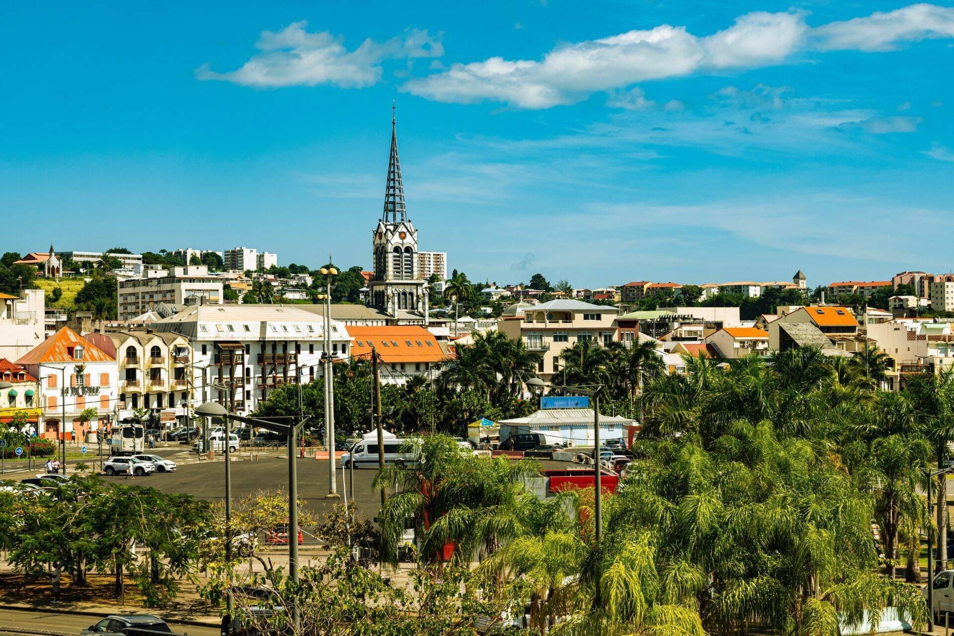Vue panoramique d’une ville côtière avec église aux toits orangés, palmiers, architecture coloniale et ciel bleu dégagé