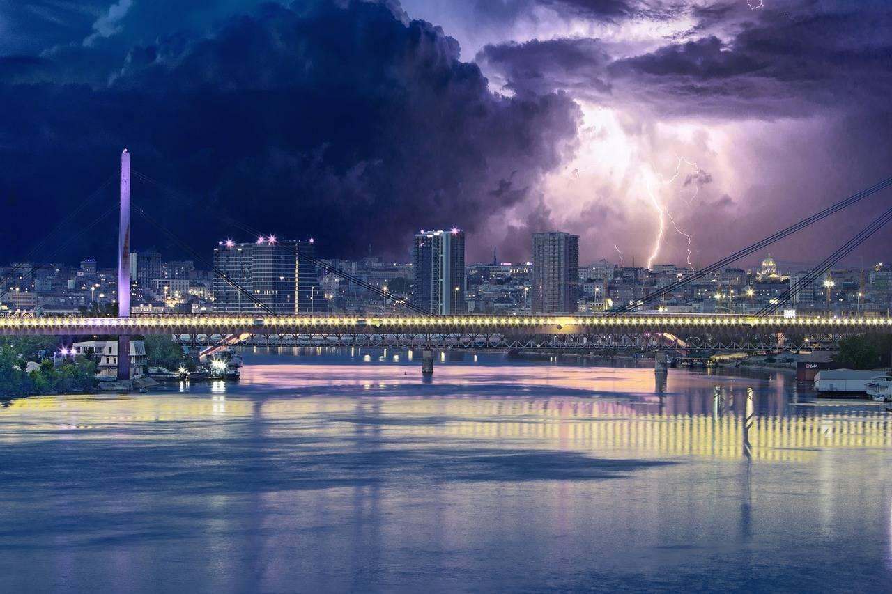 Un pont illuminé enjambant un fleuve avec une ville en arrière-plan sous un orage électrique spectaculaire