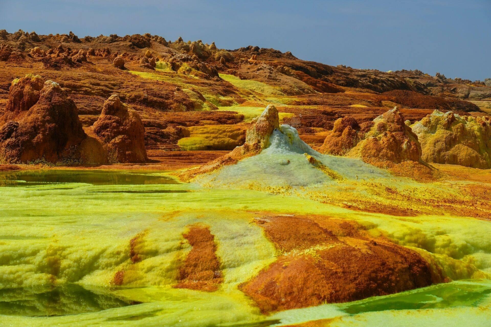 Paysage géothermique avec sources chaudes teintées de soufre jaune et roches ocre rougeâtre