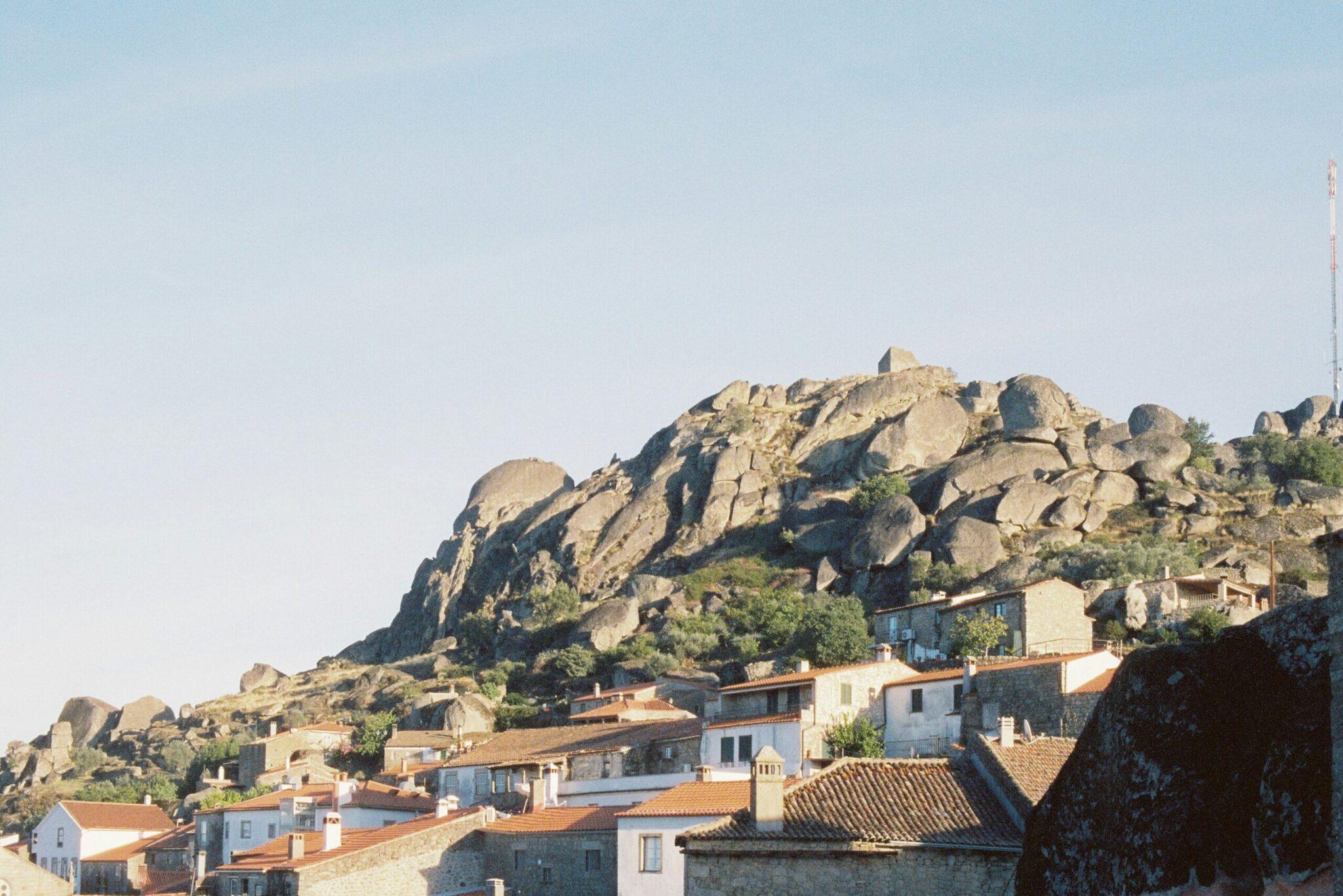 Un village aux maisons blanches et toits rouges construites à flanc d’une montagne rocheuse parsemée de boulders géants