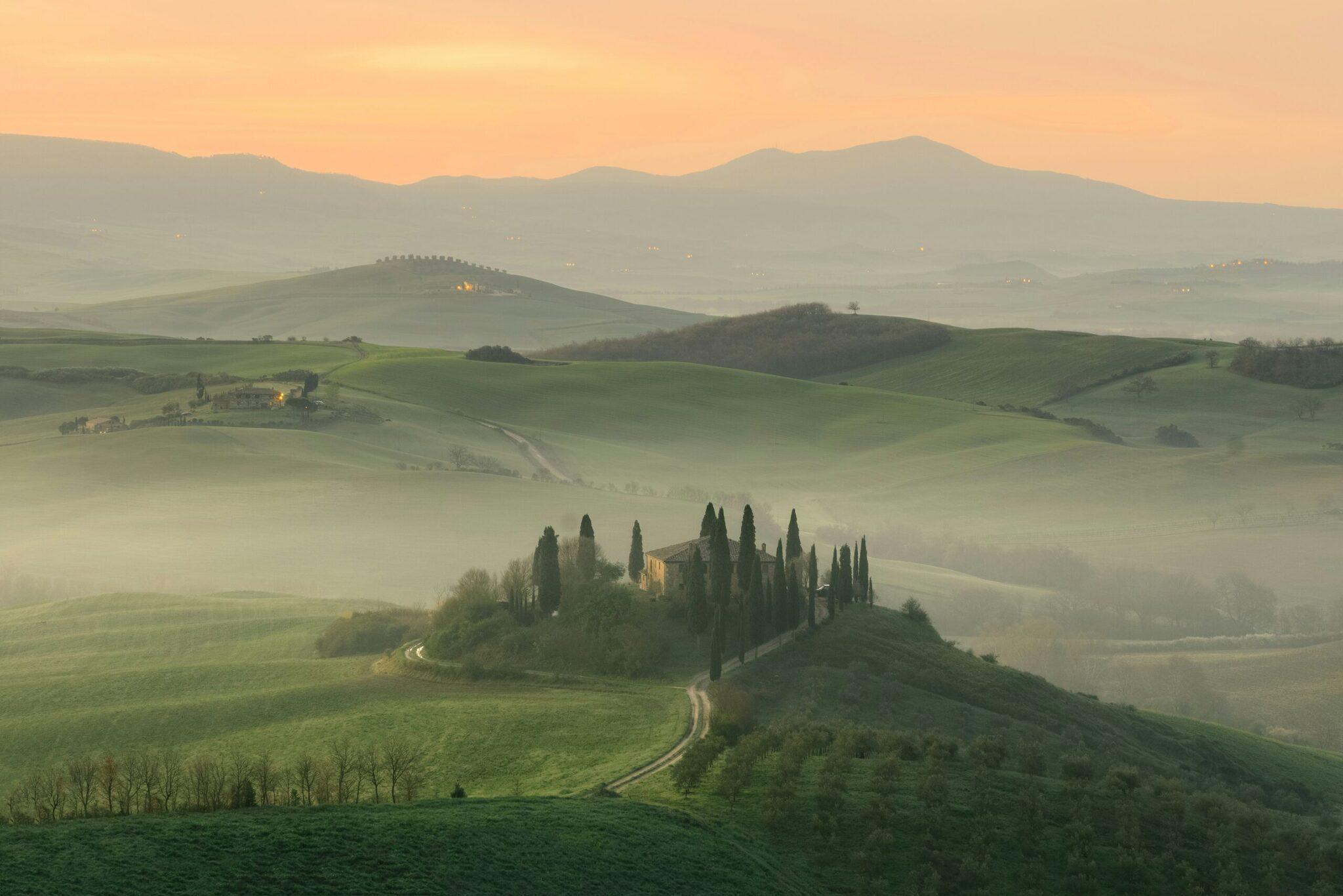 Une villa toscane entourée de cyprès dans un paysage vallonné brumeux au lever du soleil