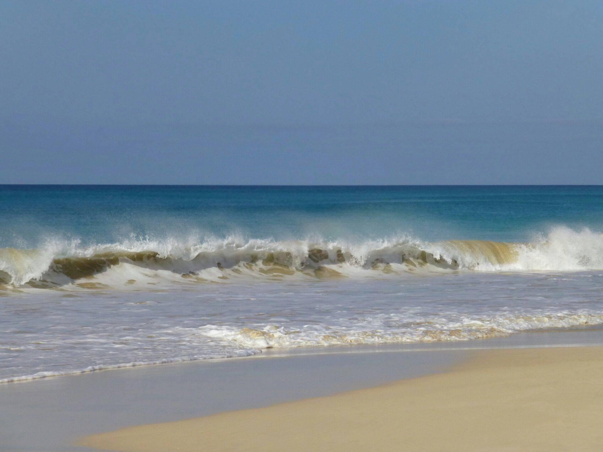 Vagues déferlantes sur une plage de sable fin sous un ciel bleu dégagé, ambiance océanique paisible