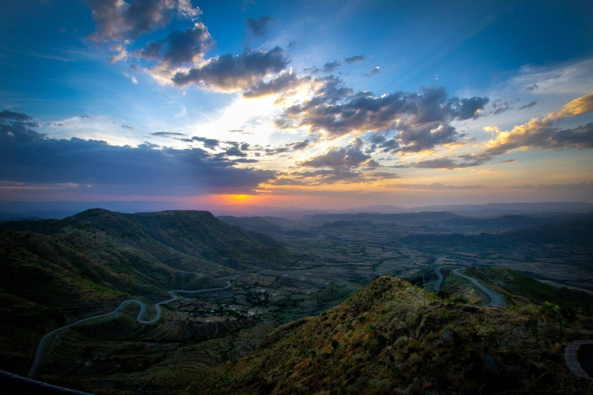 Vallée fluviale sinueuse encadrée de collines verdoyantes au coucher de soleil, paysage montagneux africain