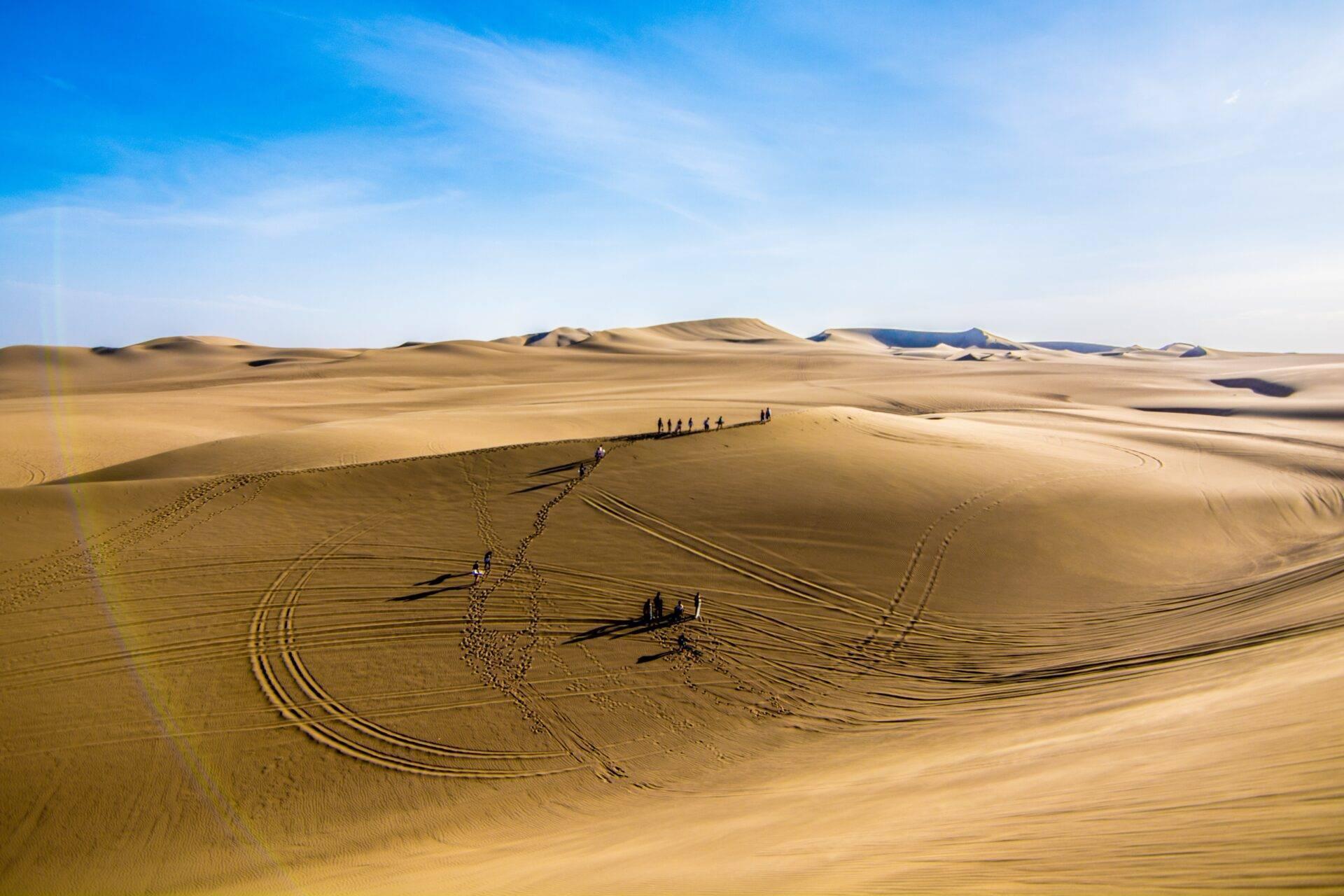 Des voyageurs marchent en caravane à travers les dunes de sable d’un vaste désert aride sous un ciel bleu