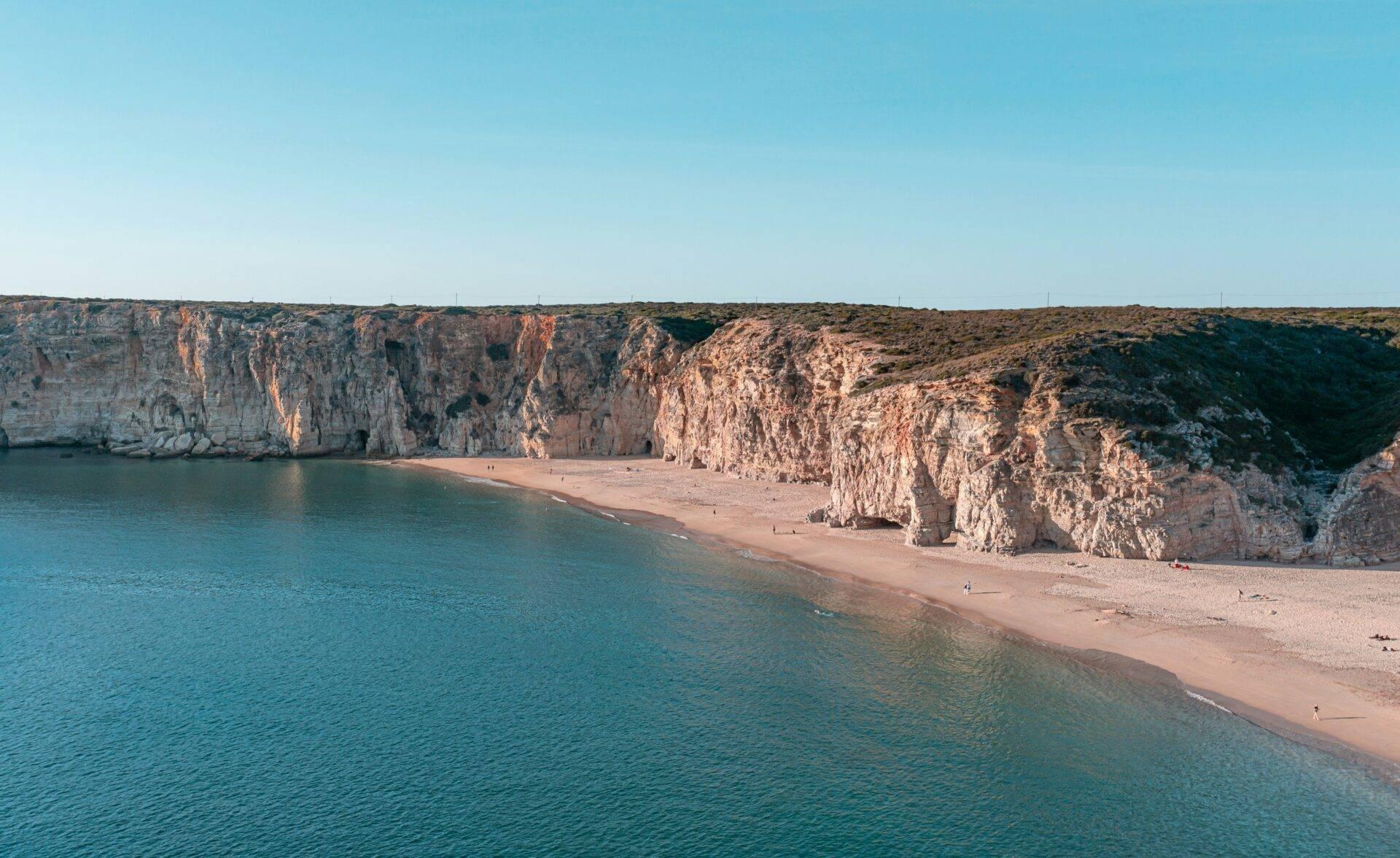 Une plage de sable fin encadrée par d’imposantes falaises calcaires blanches surplombant une mer turquoise cristalline