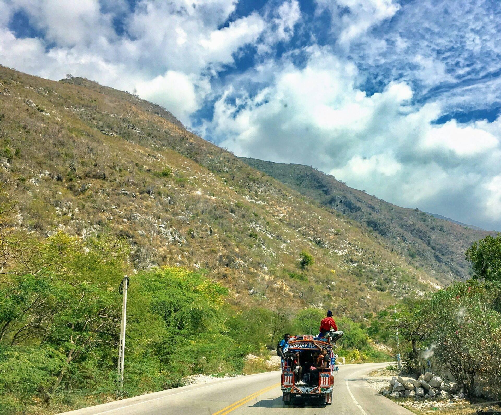 Un camion coloré circulant sur une route de montagne entourée de végétation luxuriante et de collines boisées