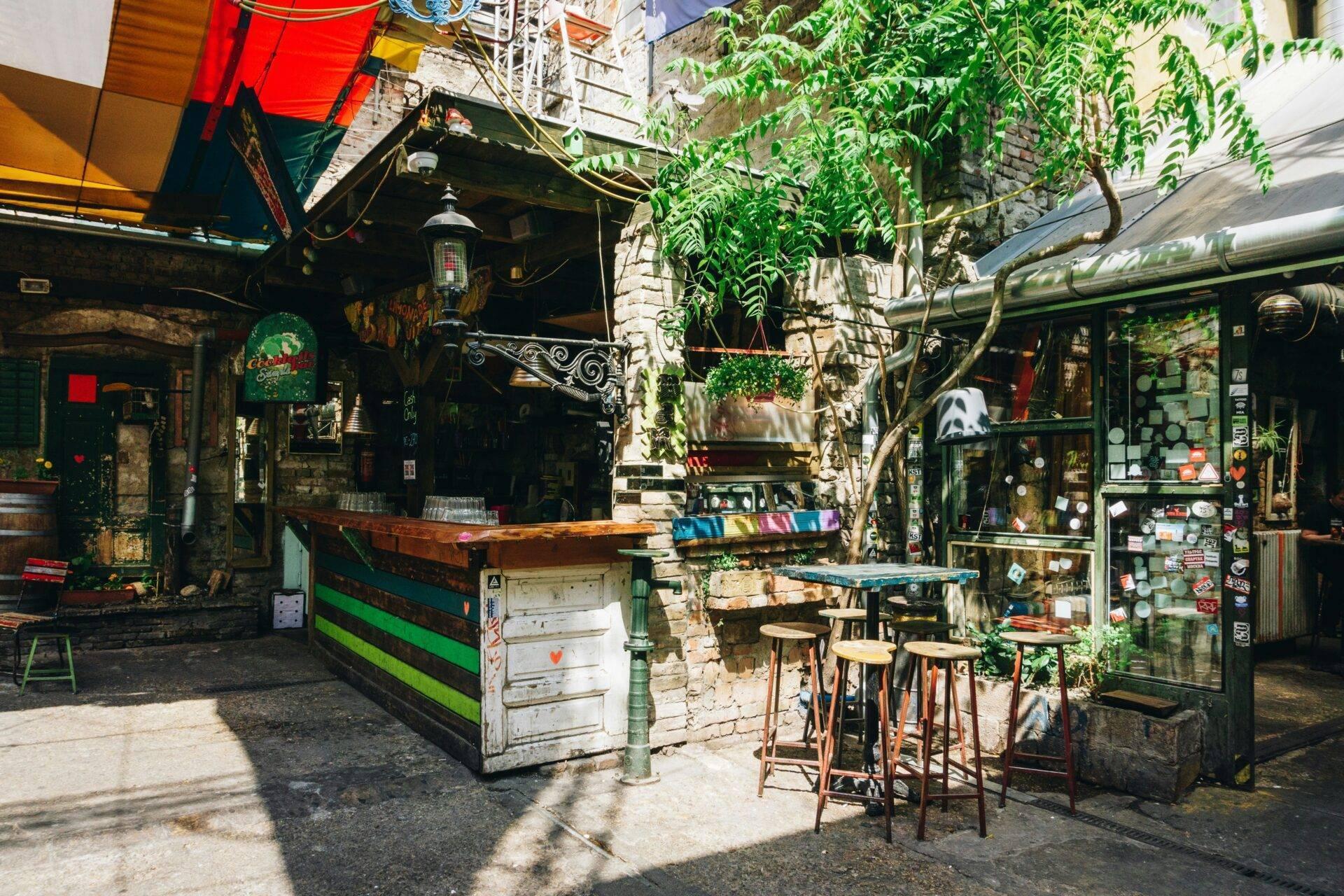 Une cour intérieure bohème avec bar coloré, végétation grimpante et mobilier vintage dans une ambiance urbaine alternative