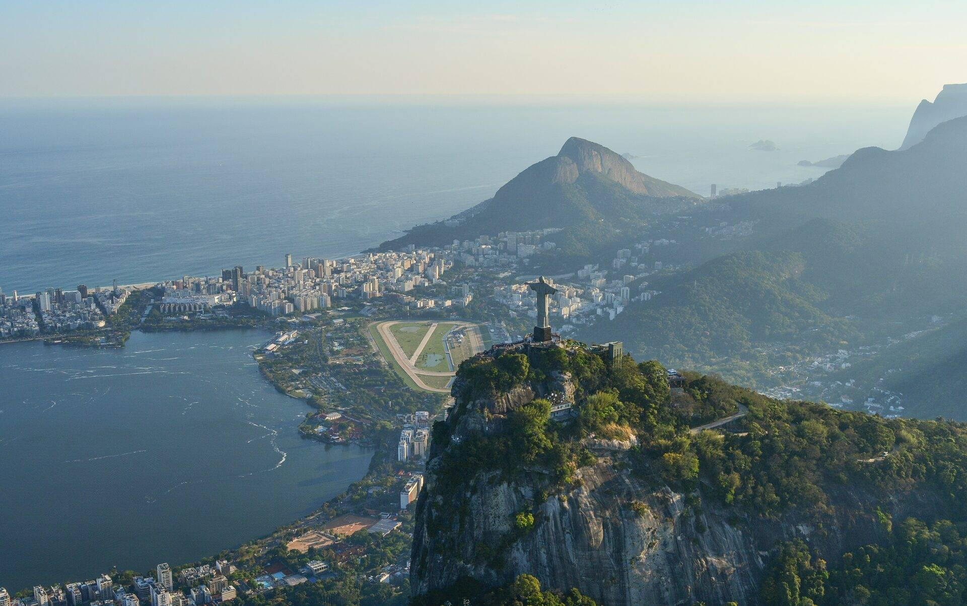 Vue aérienne d’une baie côtière avec un monument iconique sur un pic rocheux dominant une ville étendue et des montagnes verdoyantes