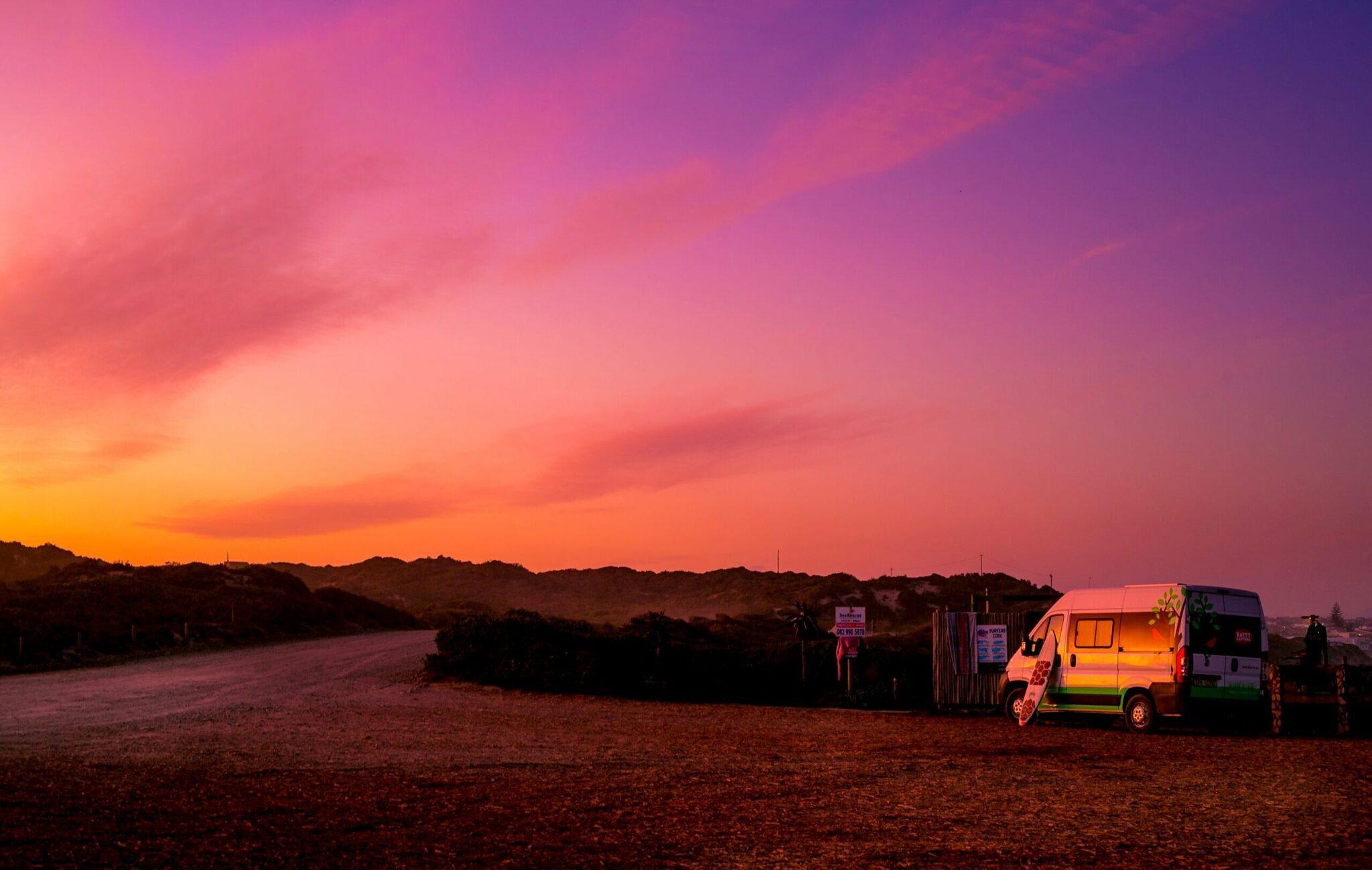 Un camping-car illuminé au coucher du soleil dans un paysage désertique avec ciel rose et orange