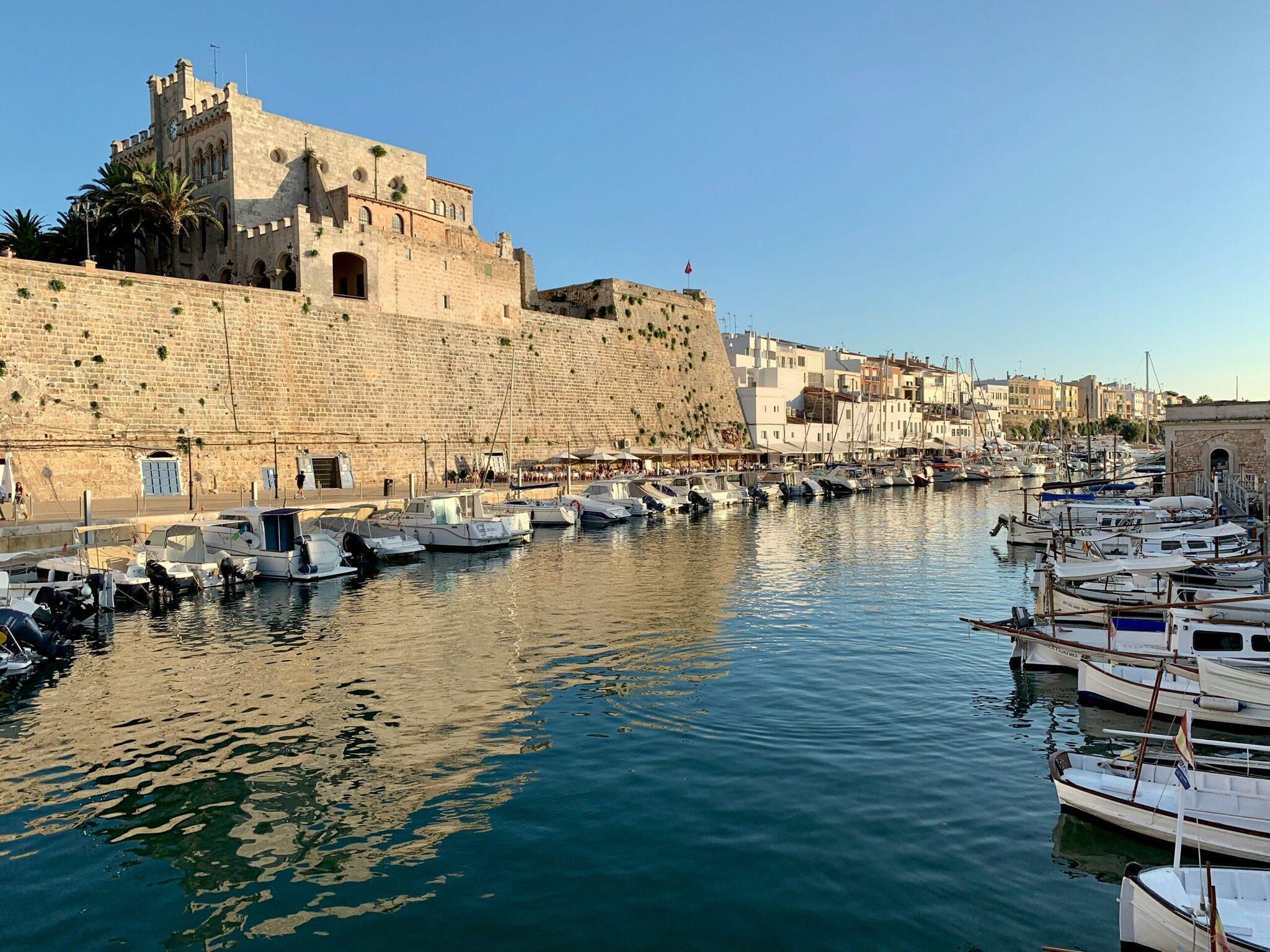 Un port méditerranéen avec une forteresse fortifiée dominant des bateaux de pêche amarrés dans une baie cristalline