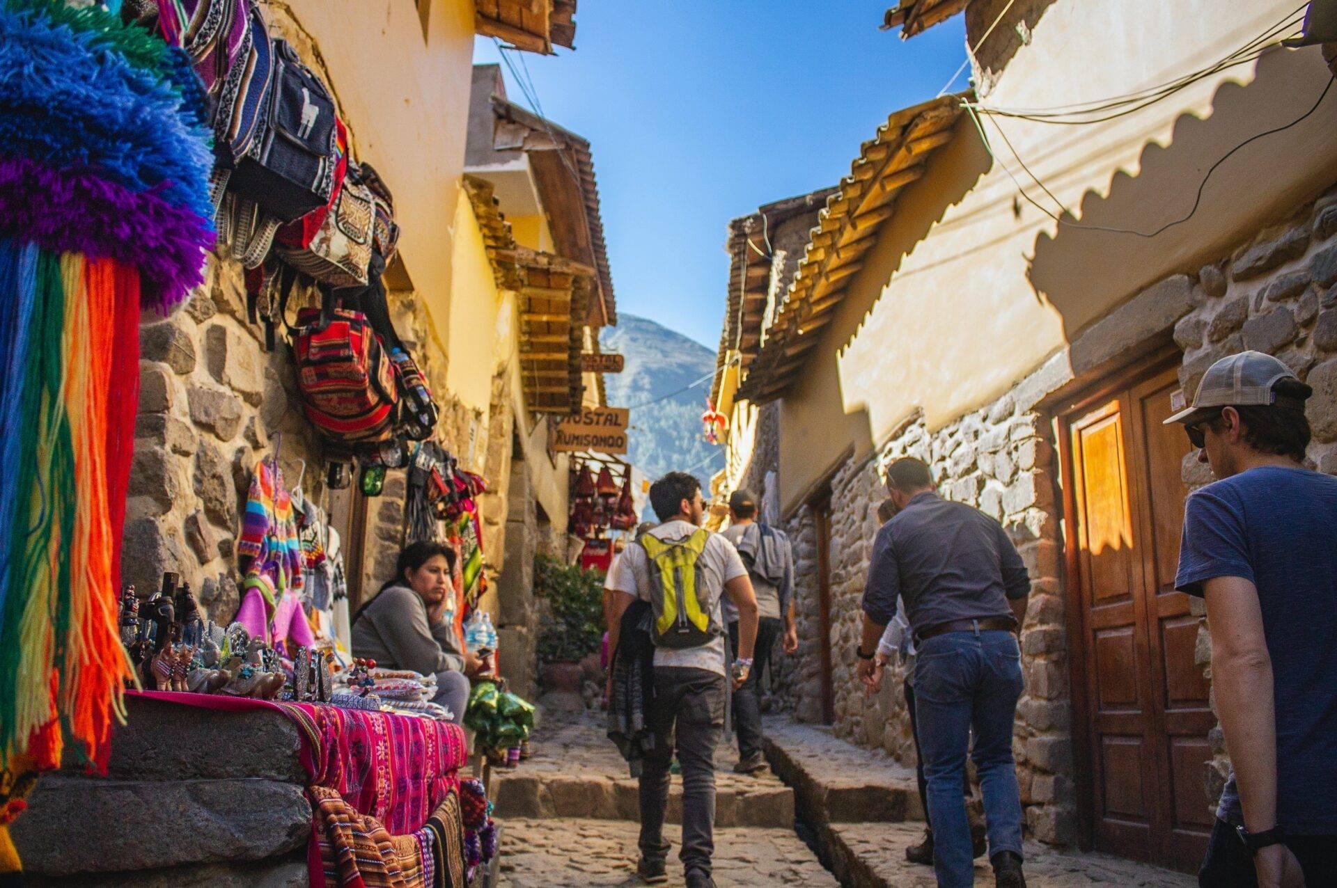 Une rue pavée étroite en pierre avec des boutiques de textiles colorés et des touristes marchant sous des toits décorés en bois