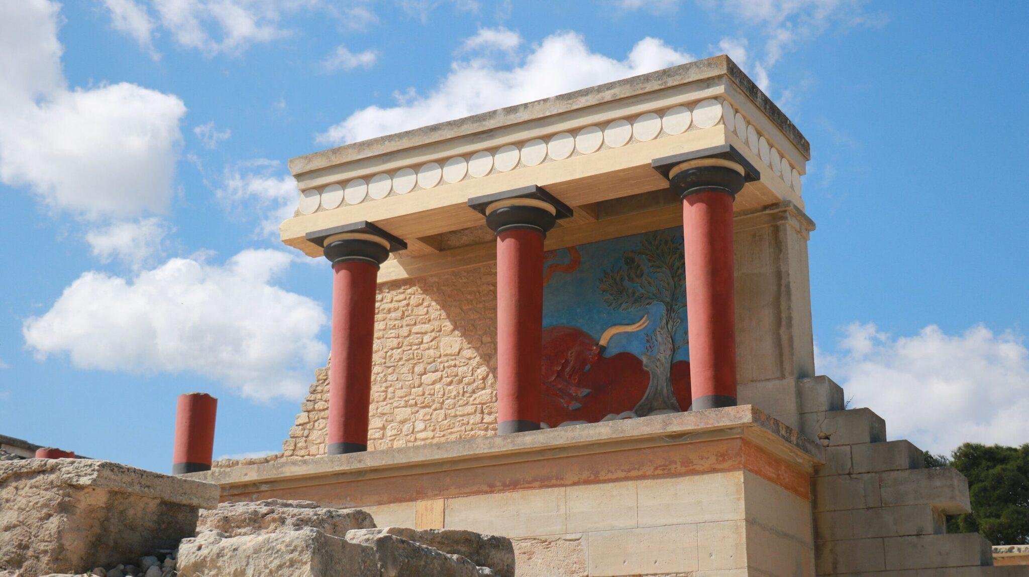 Reconstructed ancient Minoan palace with red inverted columns and colourful wall frescoes under a clear sky