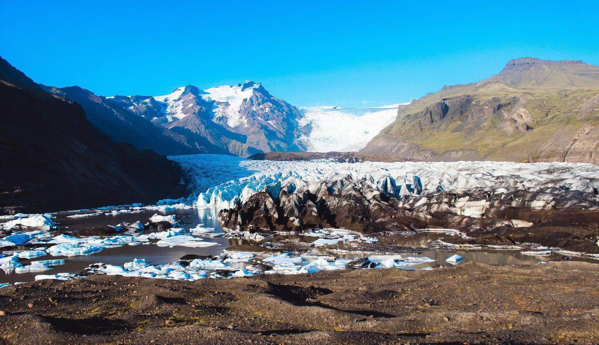 Un glacier blanc et bleu encadré de montagnes rocheuses avec des glaçons flottant dans un lac glaciaire