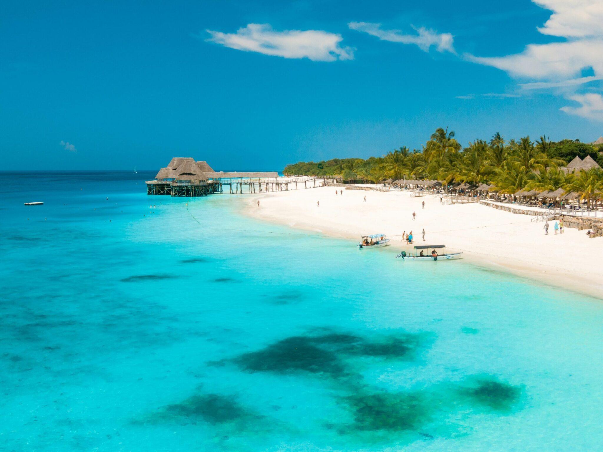 Plage tropicale paradisiaque avec eau turquoise cristalline, bungalow sur pilotis, palmiers et touristes au sable blanc