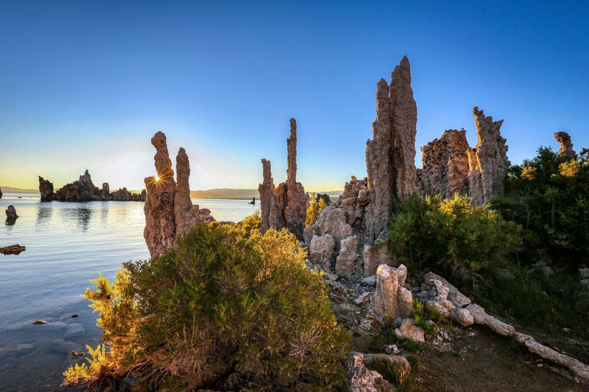 Des formations rocheuses en colonnes émergeant d’une baie côtière au coucher du soleil, avec végétation verte