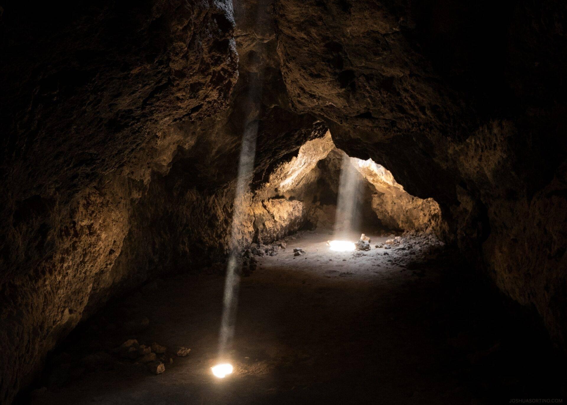 Intérieur d’une grotte rocheuse avec rayons de lumière traversant l’obscurité et sol rocheux illuminé