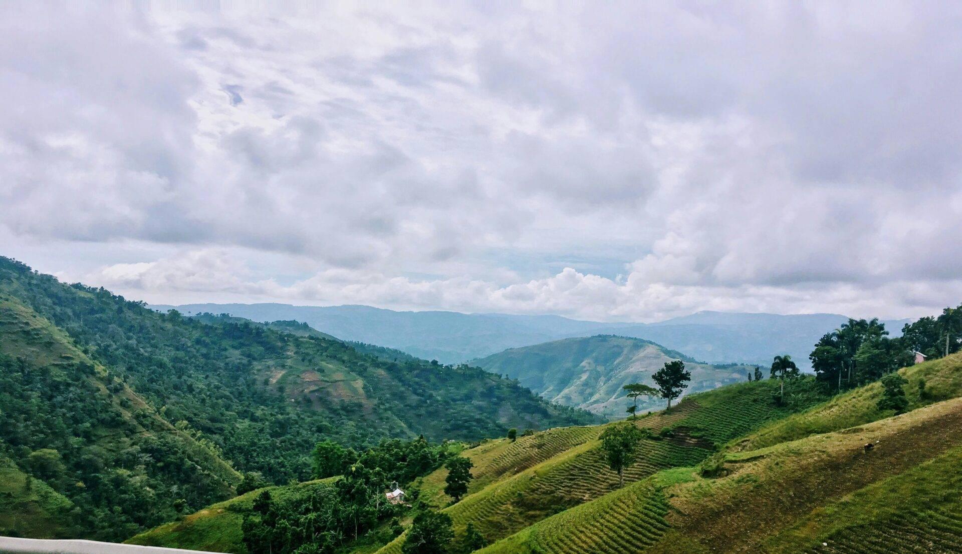 Vallées verdoyantes et collines cultivées avec maisons dispersées sous un ciel nuageux en région montagneuse tropicale