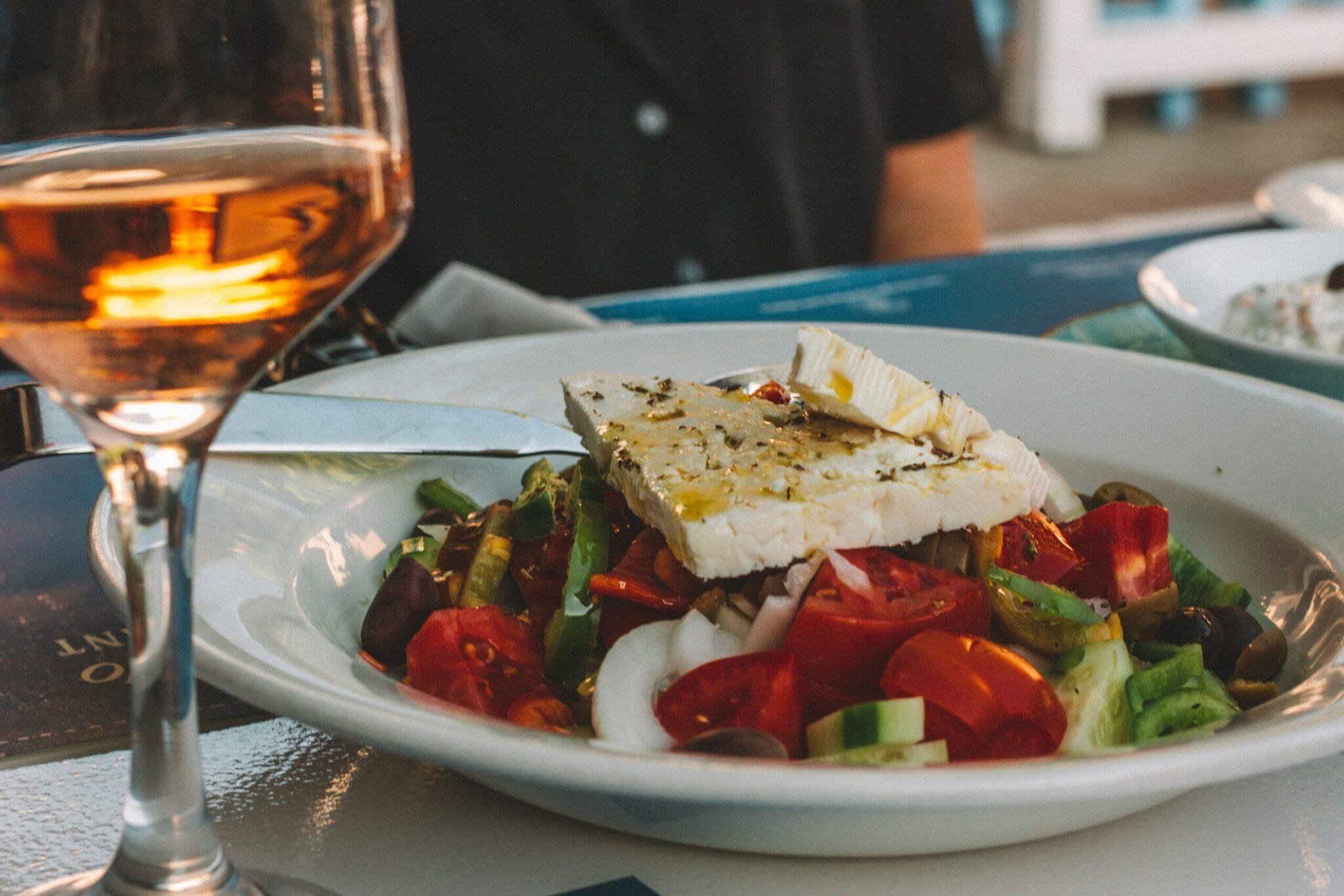 Plate of Mediterranean salad with feta and a glass of rosé wine on a sun-drenched terrace