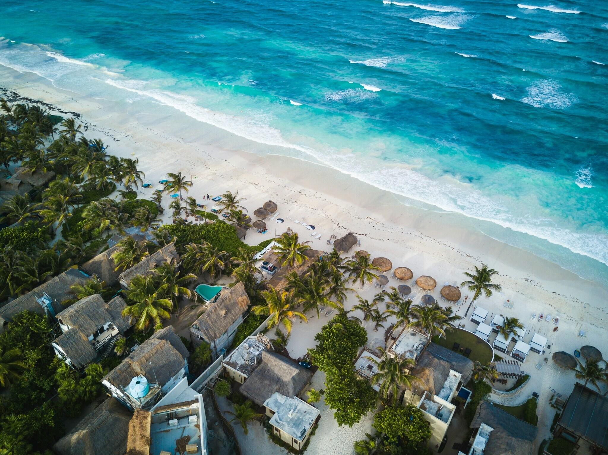 Vue aérienne d’une plage tropicale avec resort, palmiers, parasols de paille et eau turquoise