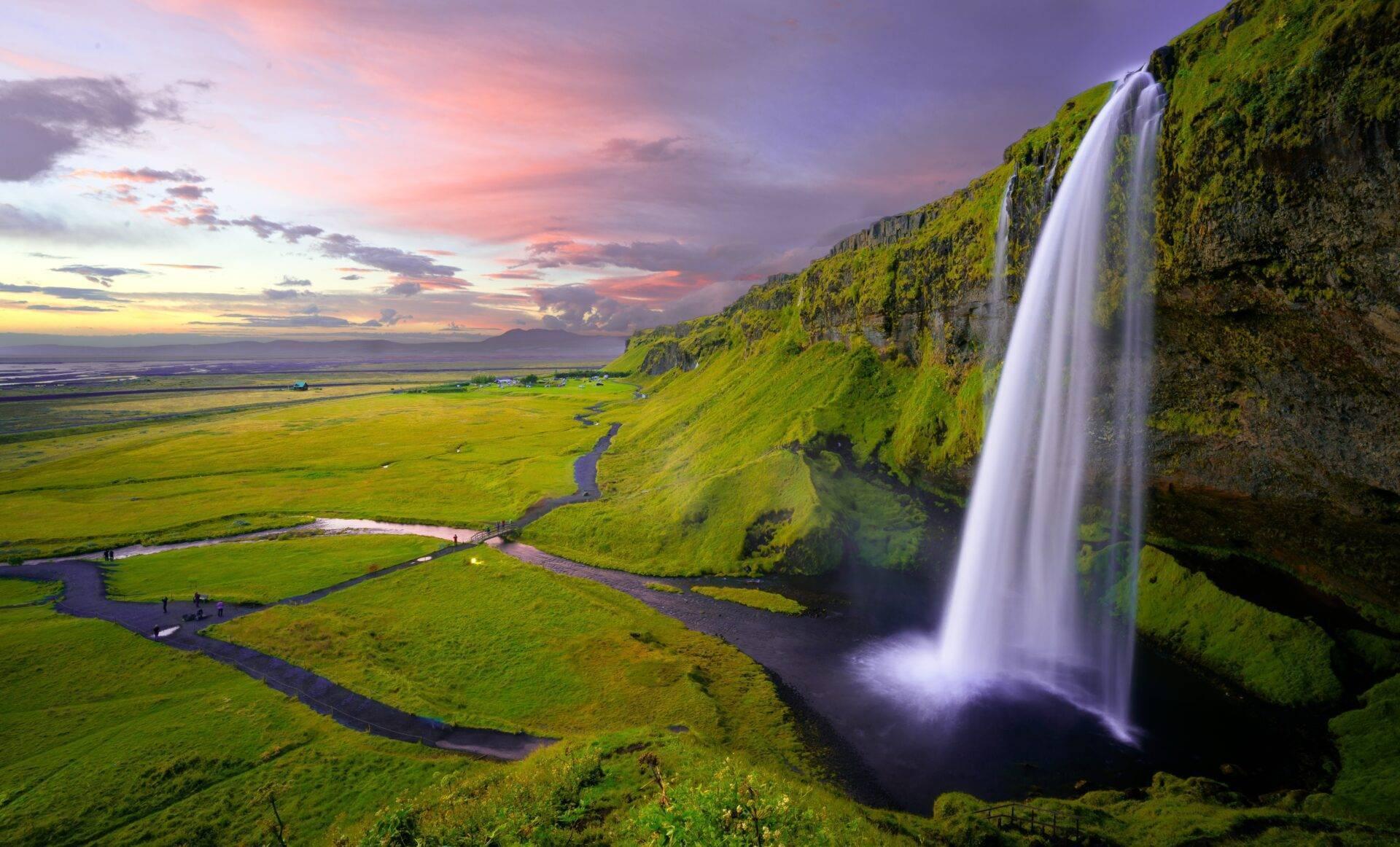 Une cascade spectaculaire déverse ses eaux sur une falaise verdoyante dominant une vallée fluviale au coucher de soleil