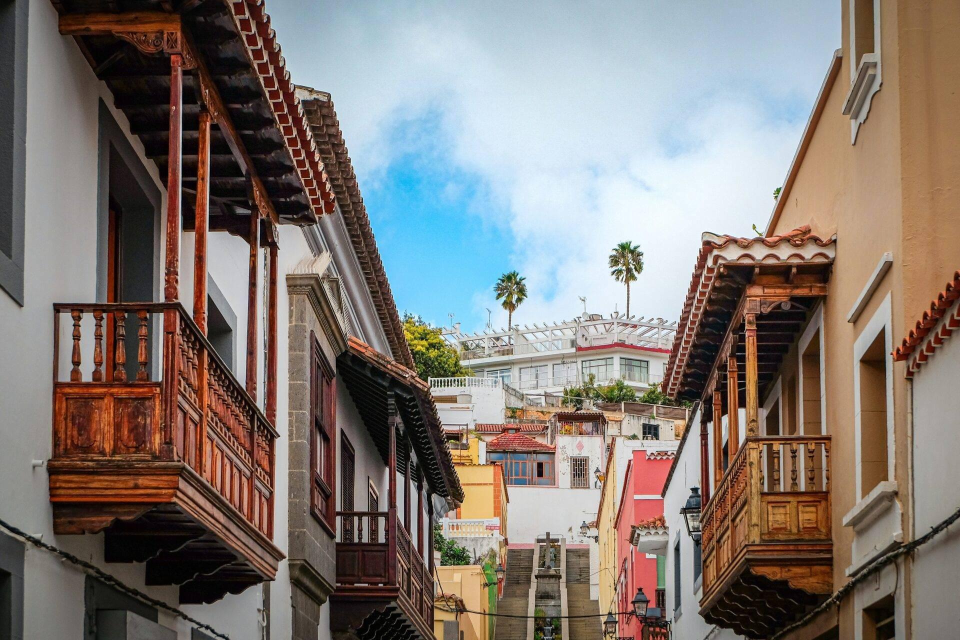 Rue pavée étroite avec balcons en bois colorés, maisons coloniales et palm trees sous ciel bleu