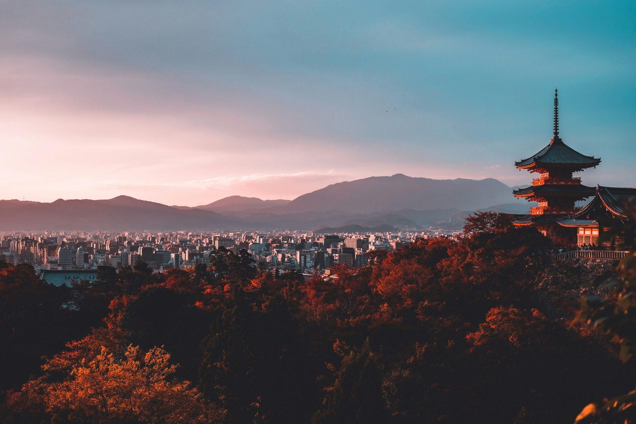 Un temple asiatique aux toits rouges domine une ville de montagne au coucher de soleil automnal