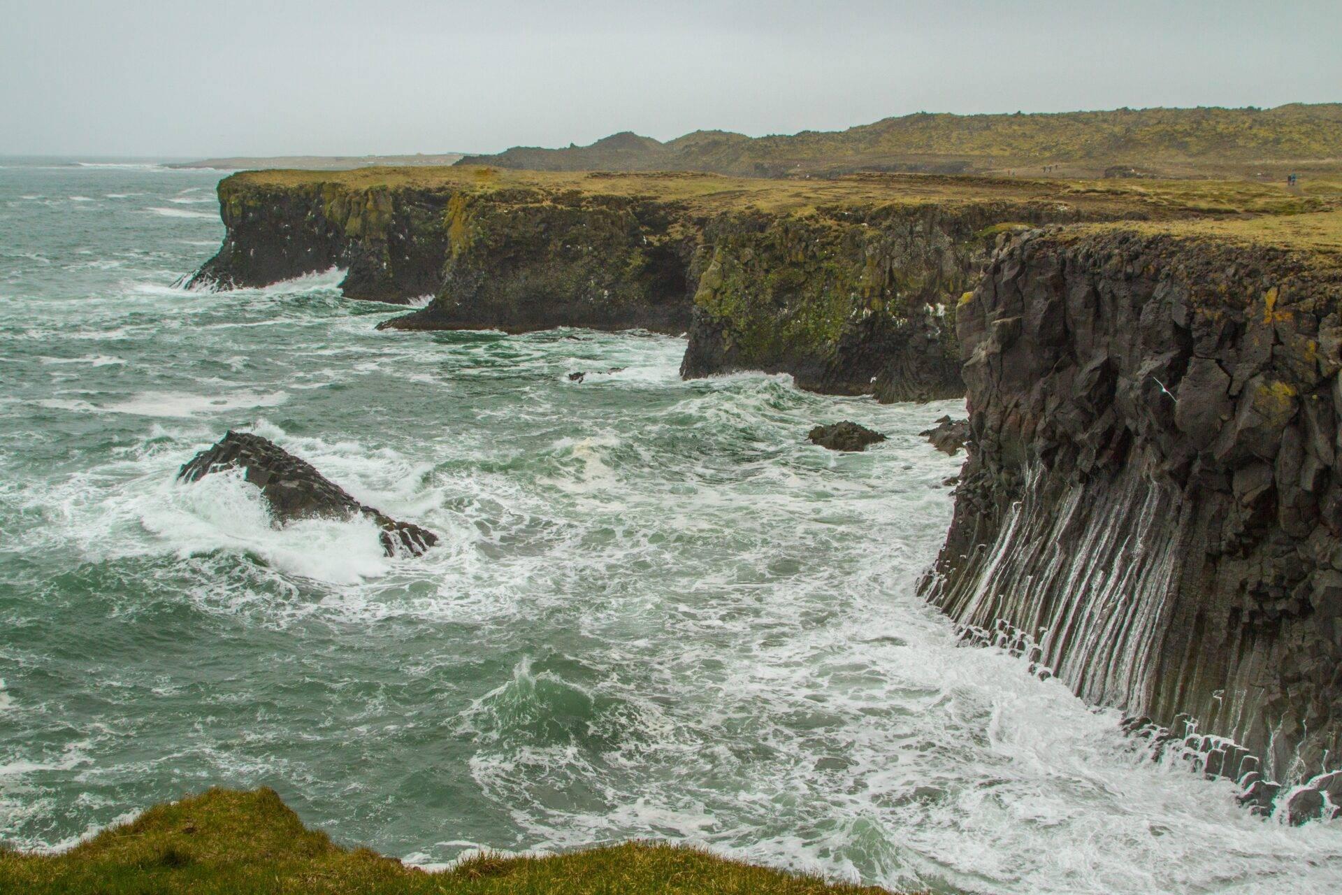 Falaises côtières en colonnes basaltiques avec mousse verte et vagues turquoises en Islande