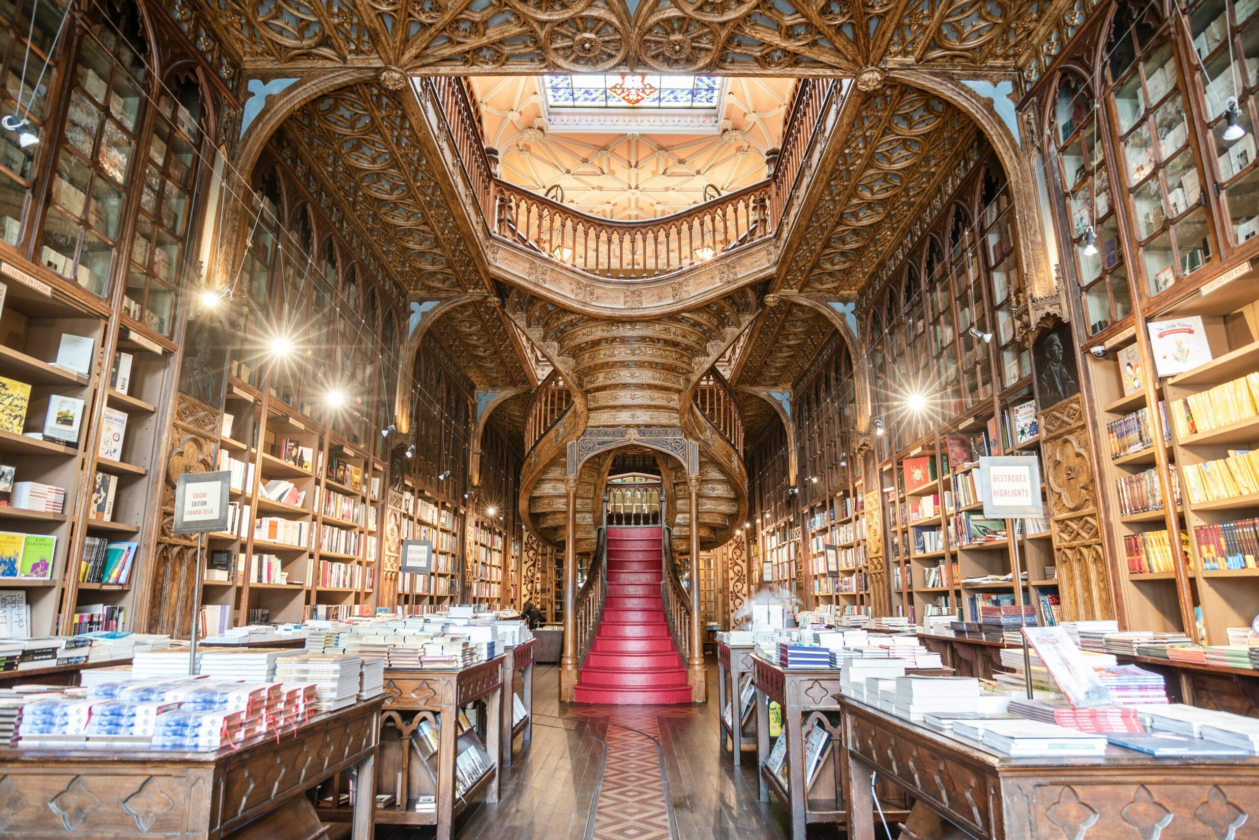 Intérieur ornementé d’une librairie historique avec plafond sculpté, rayonnages de bois et escalier rouge central
