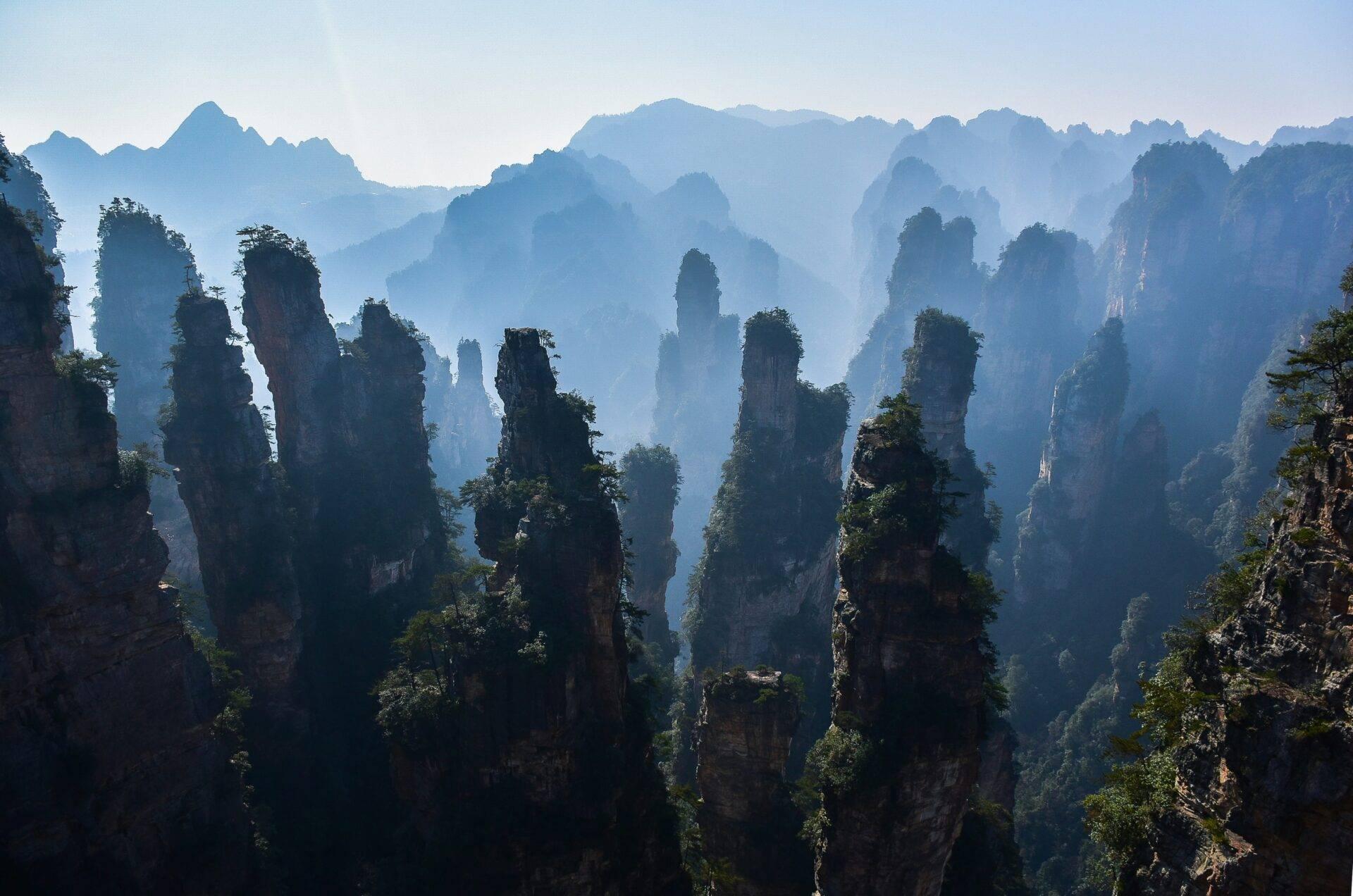 Formations rocheuses spectaculaires en grès avec végétation dense dans une vallée montagneuse enveloppée de brume bleue